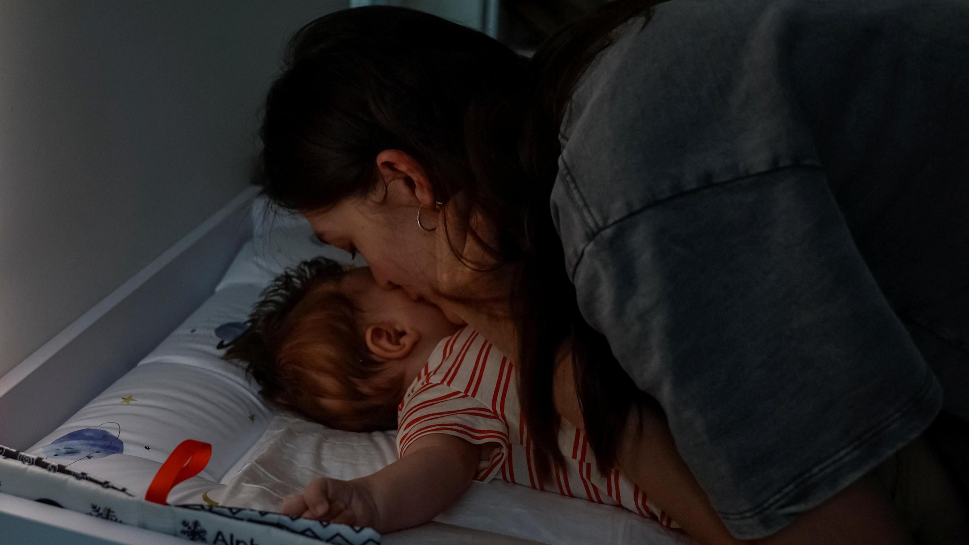 A mum kisses her baby during a blackout following a Russian attack on Ukraine's power grid. The baby is resting on a changing mat.