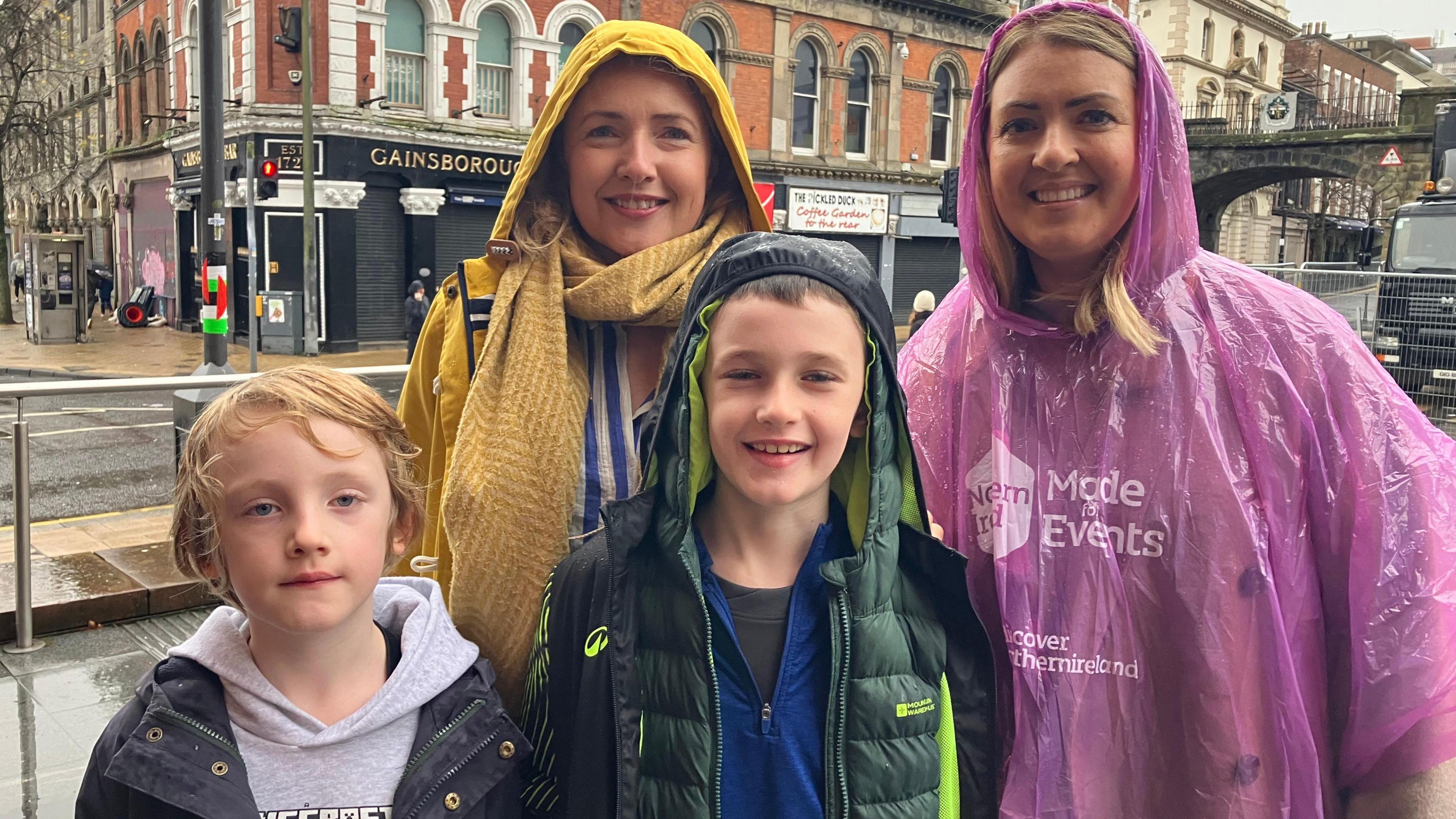 Naomi McLaughlin back left, she has light hair and is wearing a pink poncho and her sons Leo and Daniel McLaughlin who both have light hair and their aunt Ruth McLaughlin on back right, who also has light hair and is wearing a yellow coat and blue and white top.