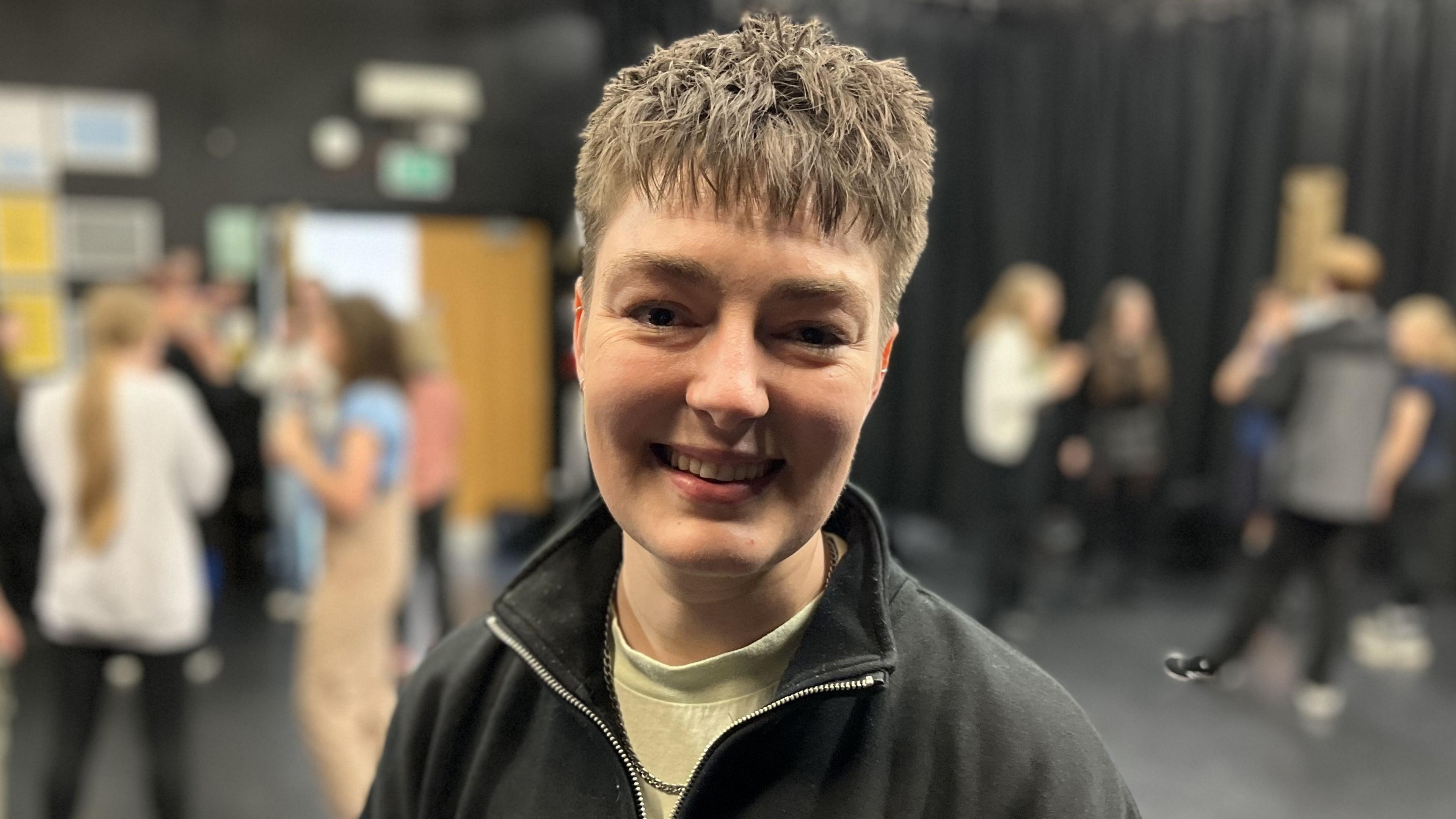 CJ Turner-McMullan with teenagers taking part in the workshop behind them, smiling with short brown hair