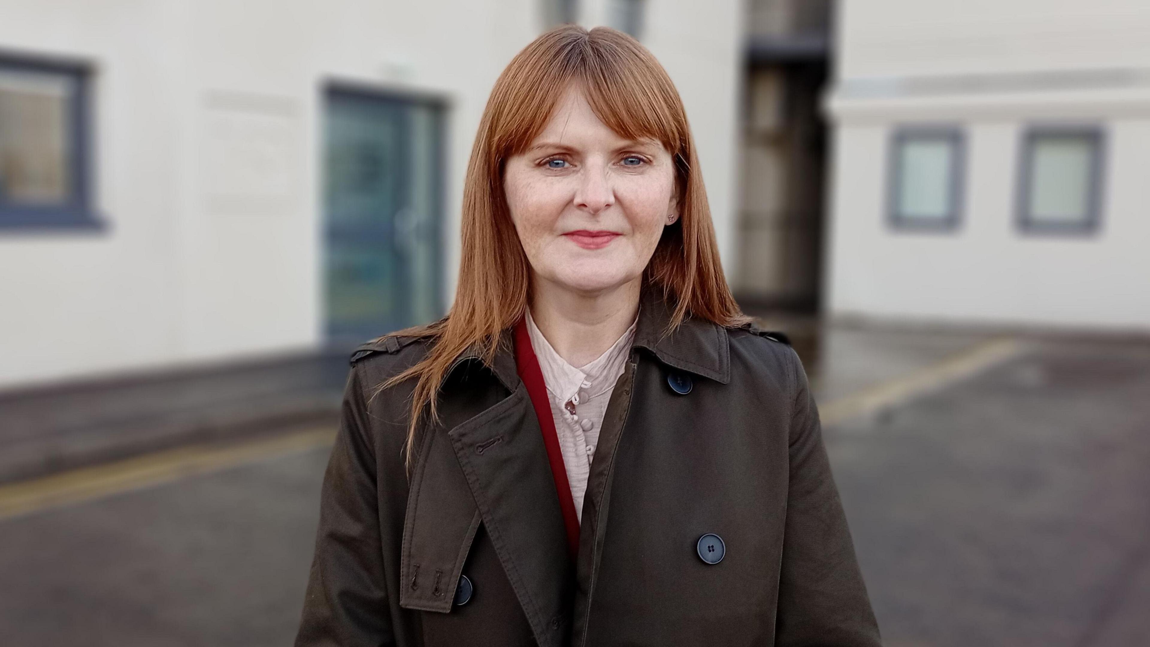 Caoimhe Archibald, a woman with long ginger hair in a green coat, stood outside an office building
