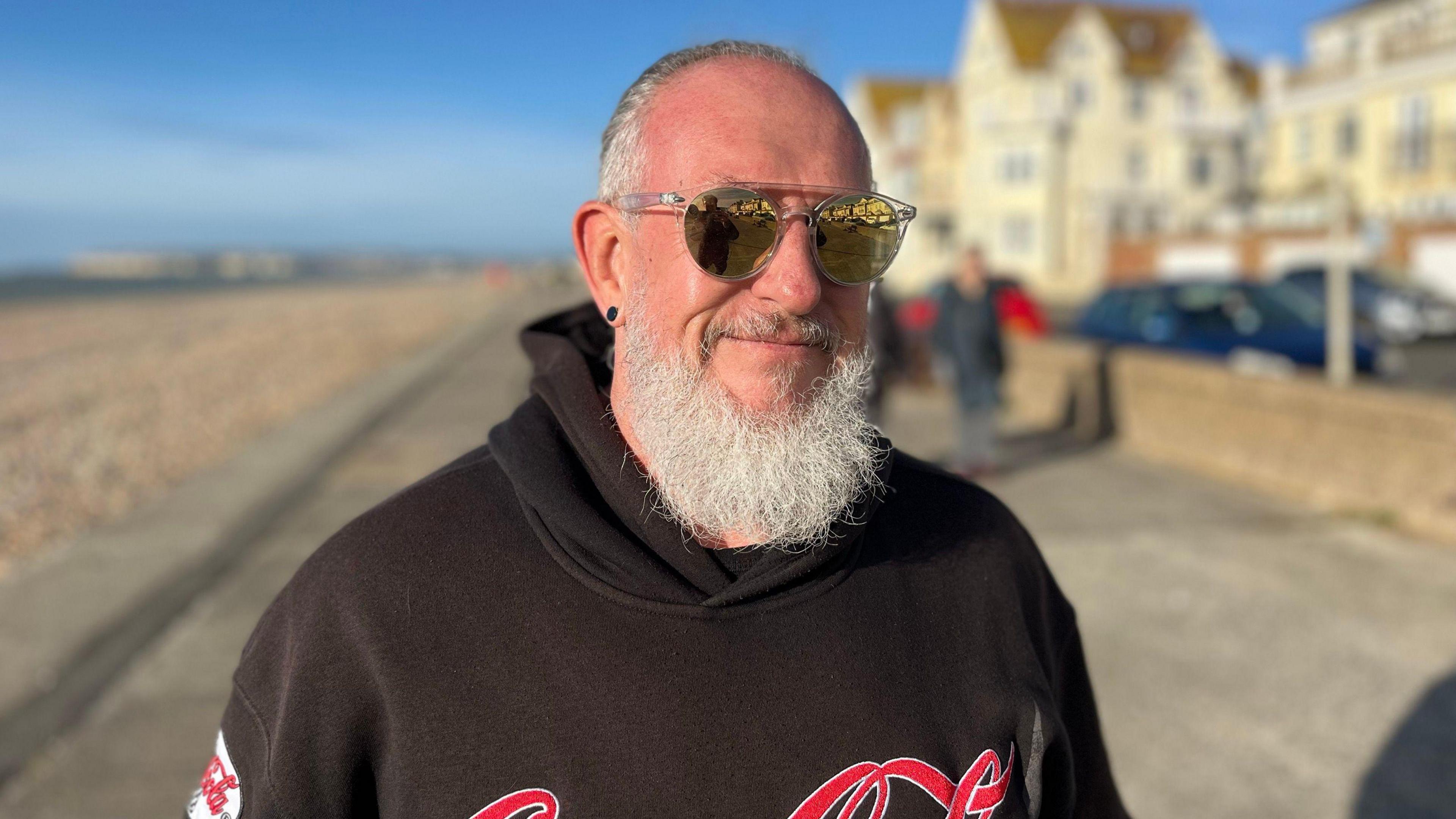 Man standing on seaford seafront wearing a coca cola hoodie and sunglasses