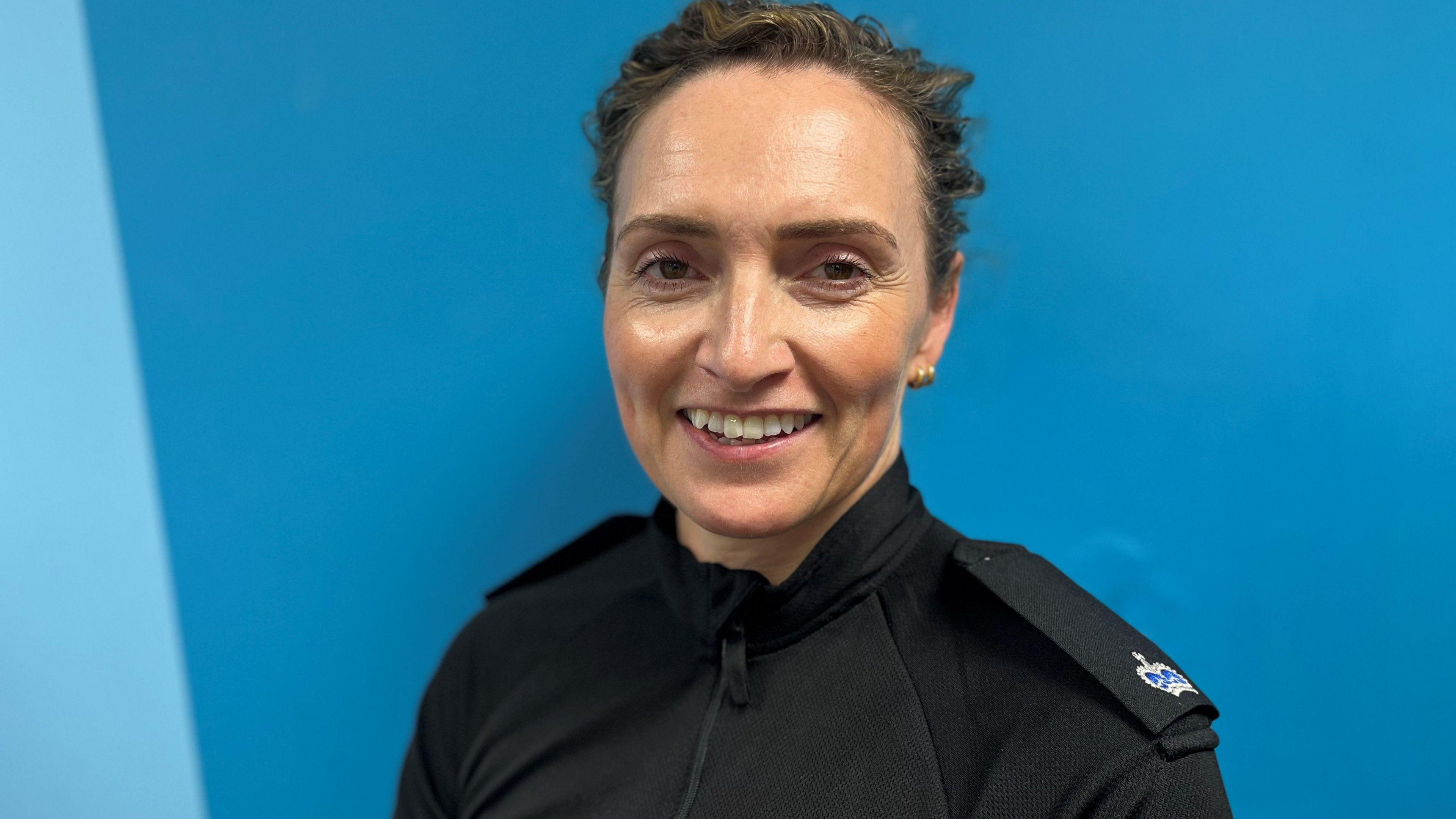 A photo of Supt Mairi MacInnes. She is looking straight at the camera wearing a black police uniform shirt with epilets. She has short brown hair.