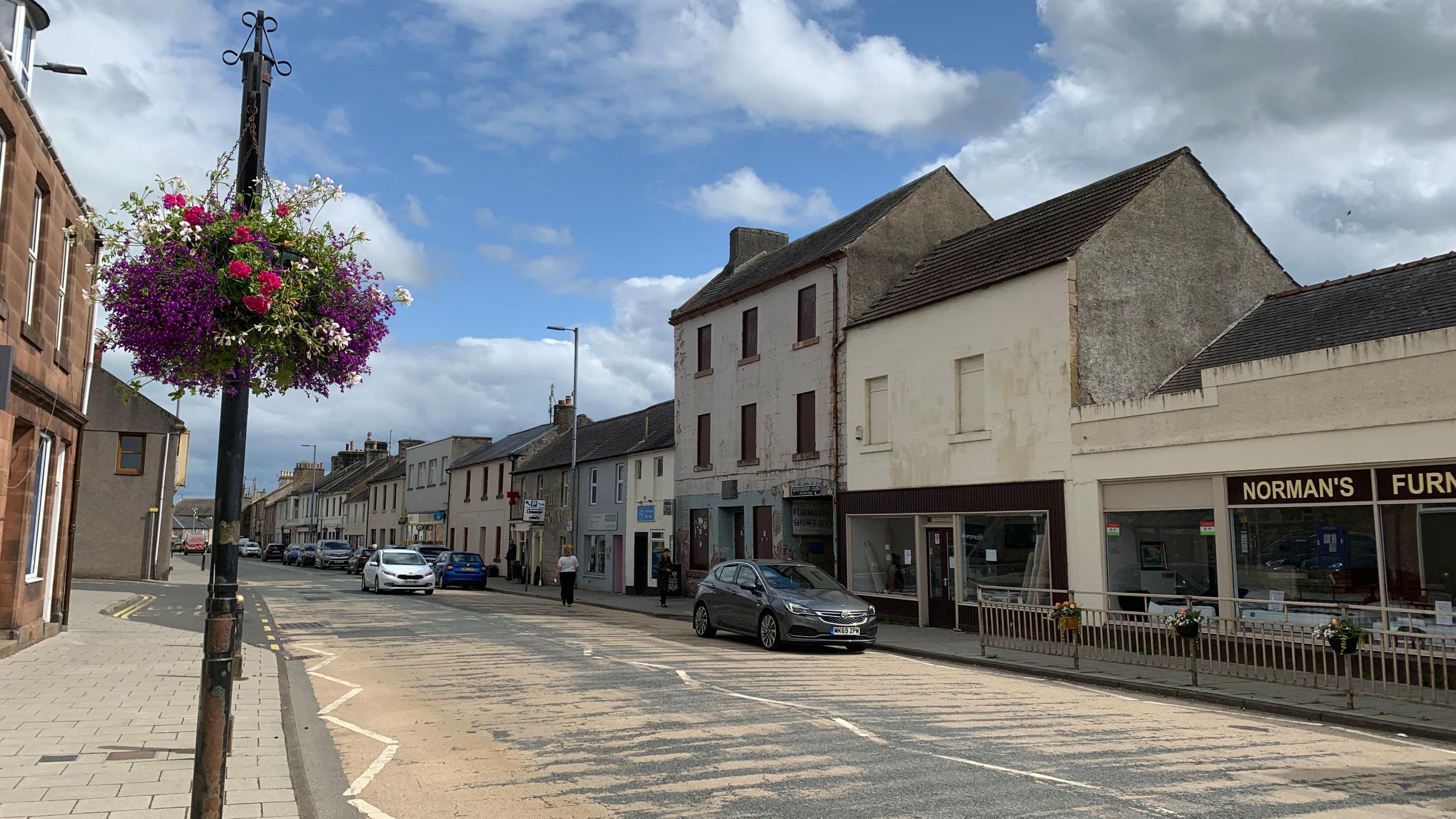 A street view of Sanquhar town centre with cars parked and a number of properties along the road