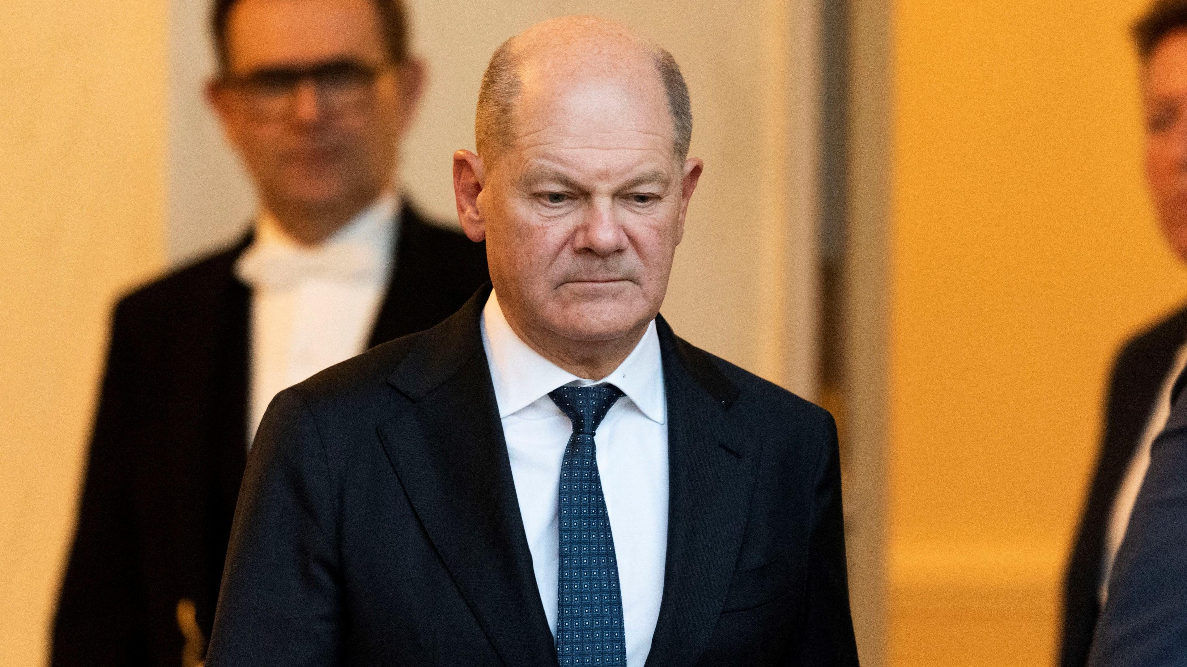 German Chancellor Olaf Scholz walks out of the Elysee Palace wearing a dark suit, white shirt and blue tie.