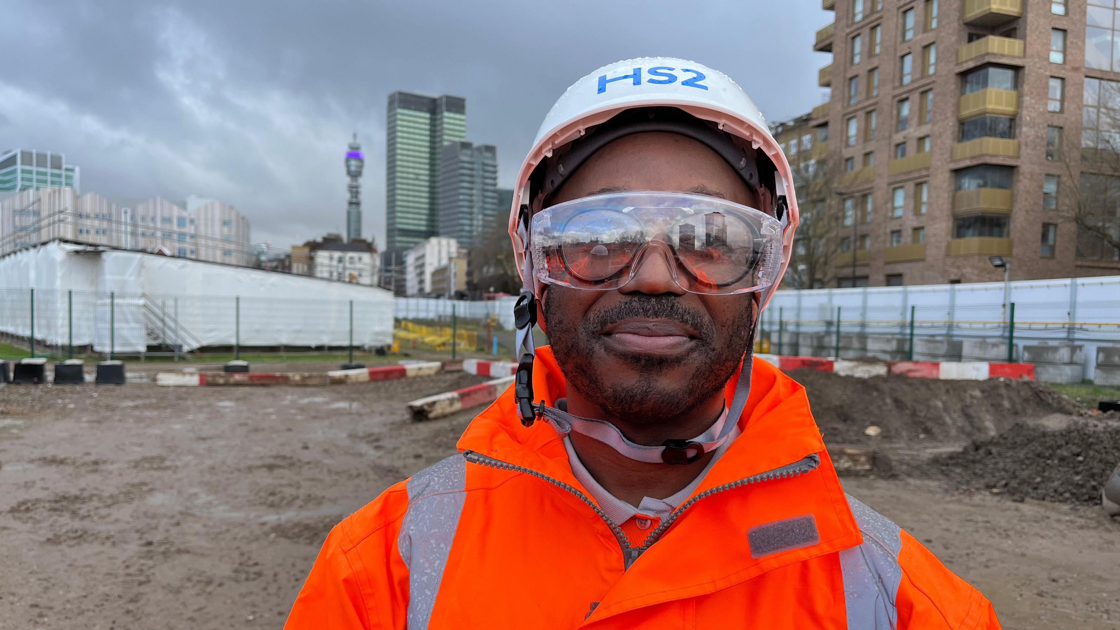 Ambrose Quashie is pictured on a building site wearing a hi-viz jacket, safety glasses and a hard hat. He is looking into the camera.