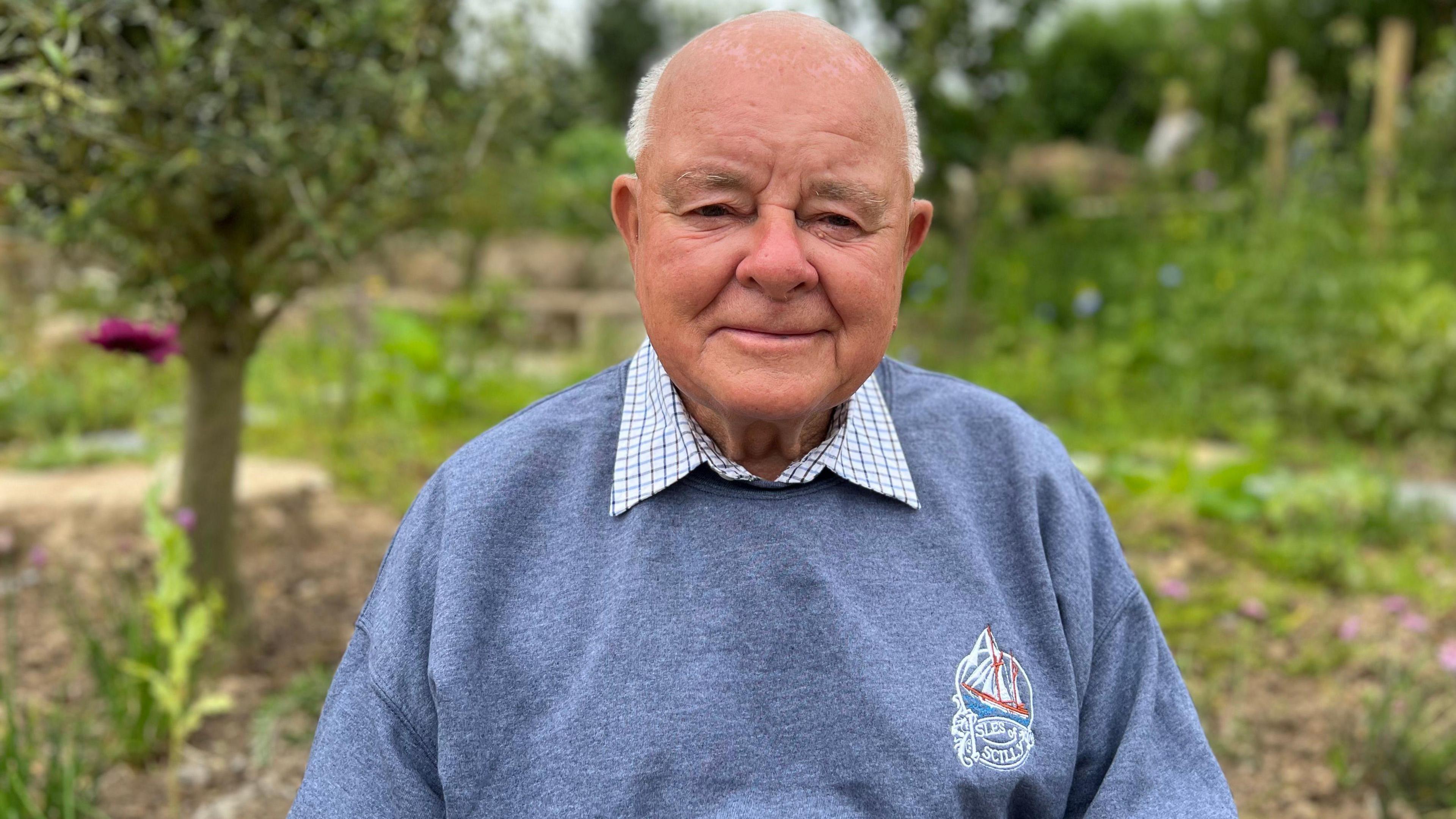 An elderly man in a blue sweatshirt smiles for the camera