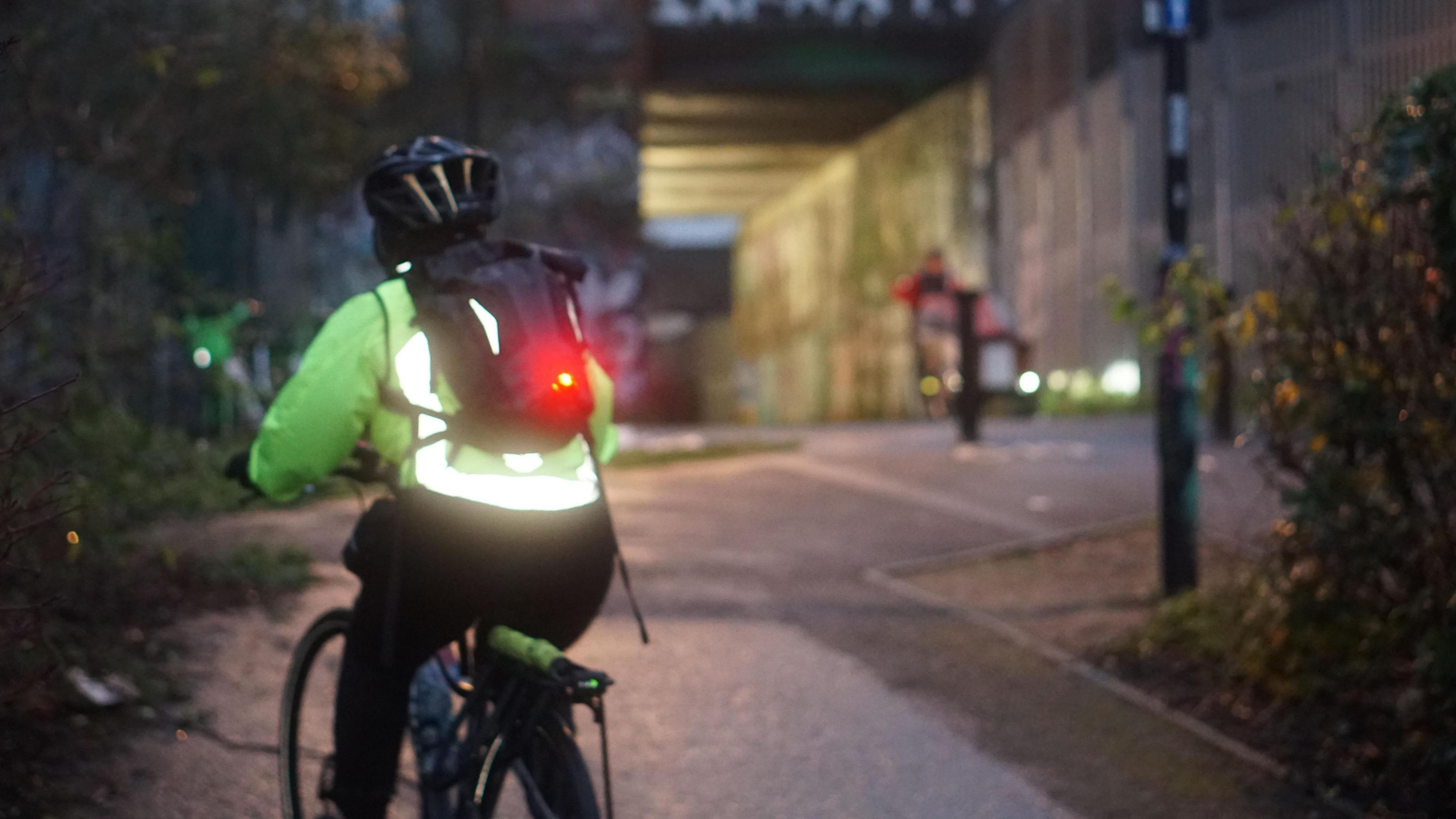 A cyclist riding away from the camera. It is dusk and the bike has lights on. An underpass is visible ahead.