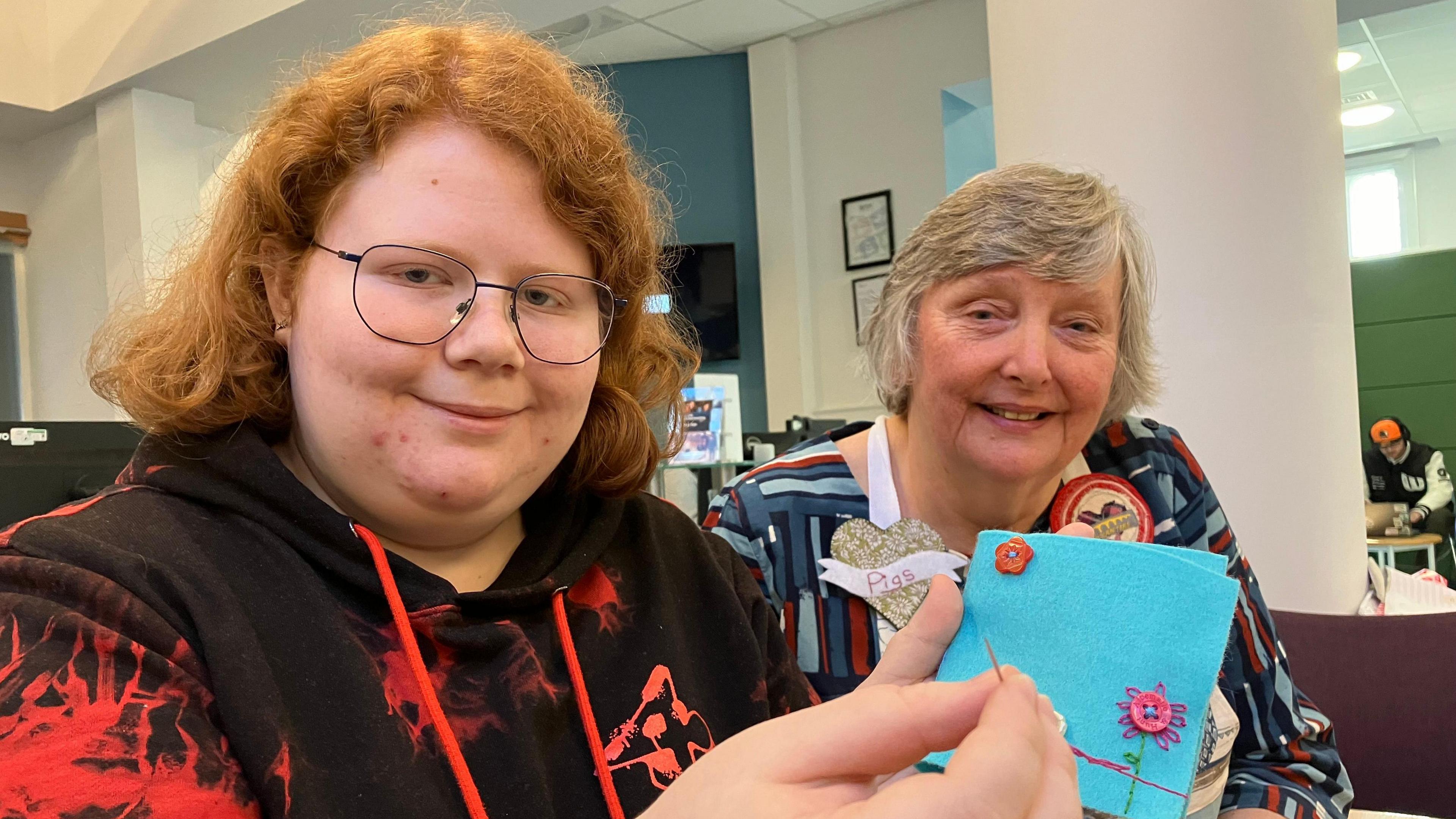 Student Abigail Attridge shows off her sewing skills, holding a piece of blue material with buttons arranged in flower patterns.