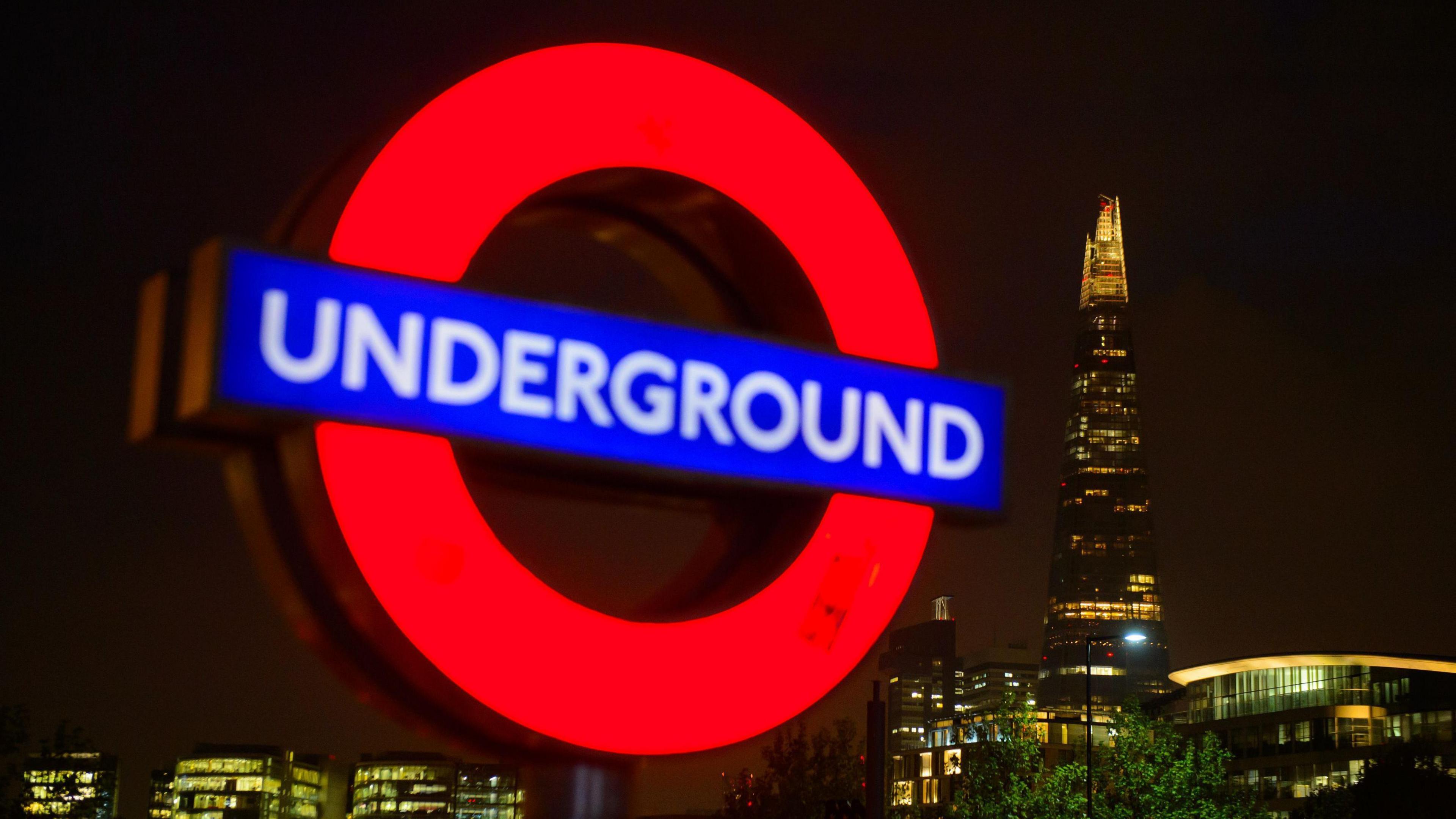 Underground sign with night time backdrop of London skyline featuring the Shard