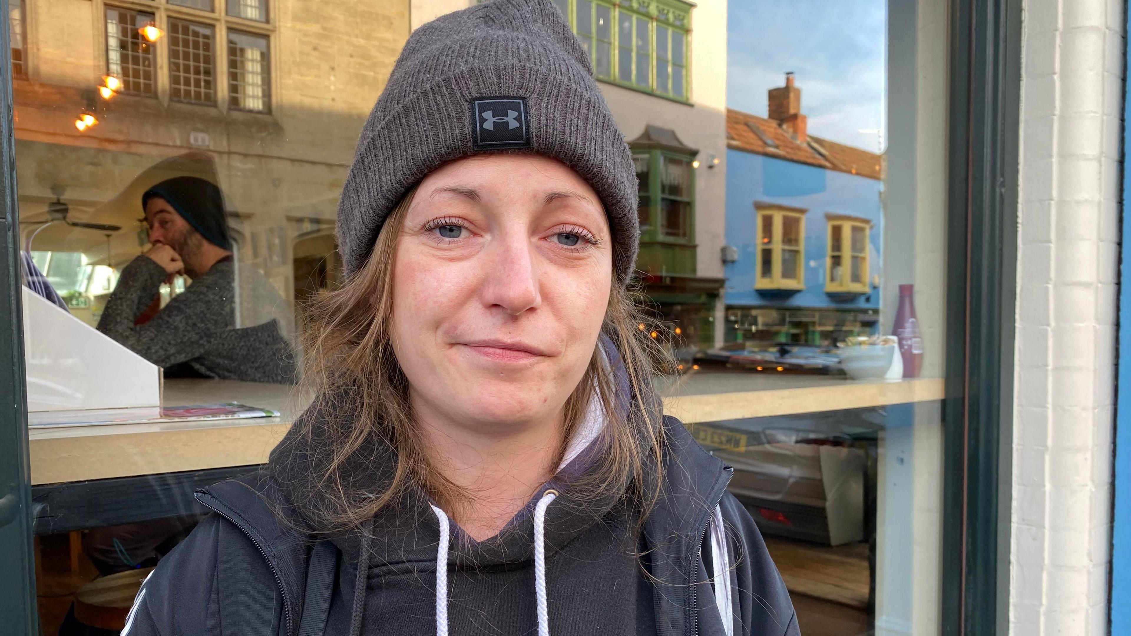 The picture shows Shannon Anderson standing outside a cafe in Glastonbury.  She is wearing a hoodie and a hat.