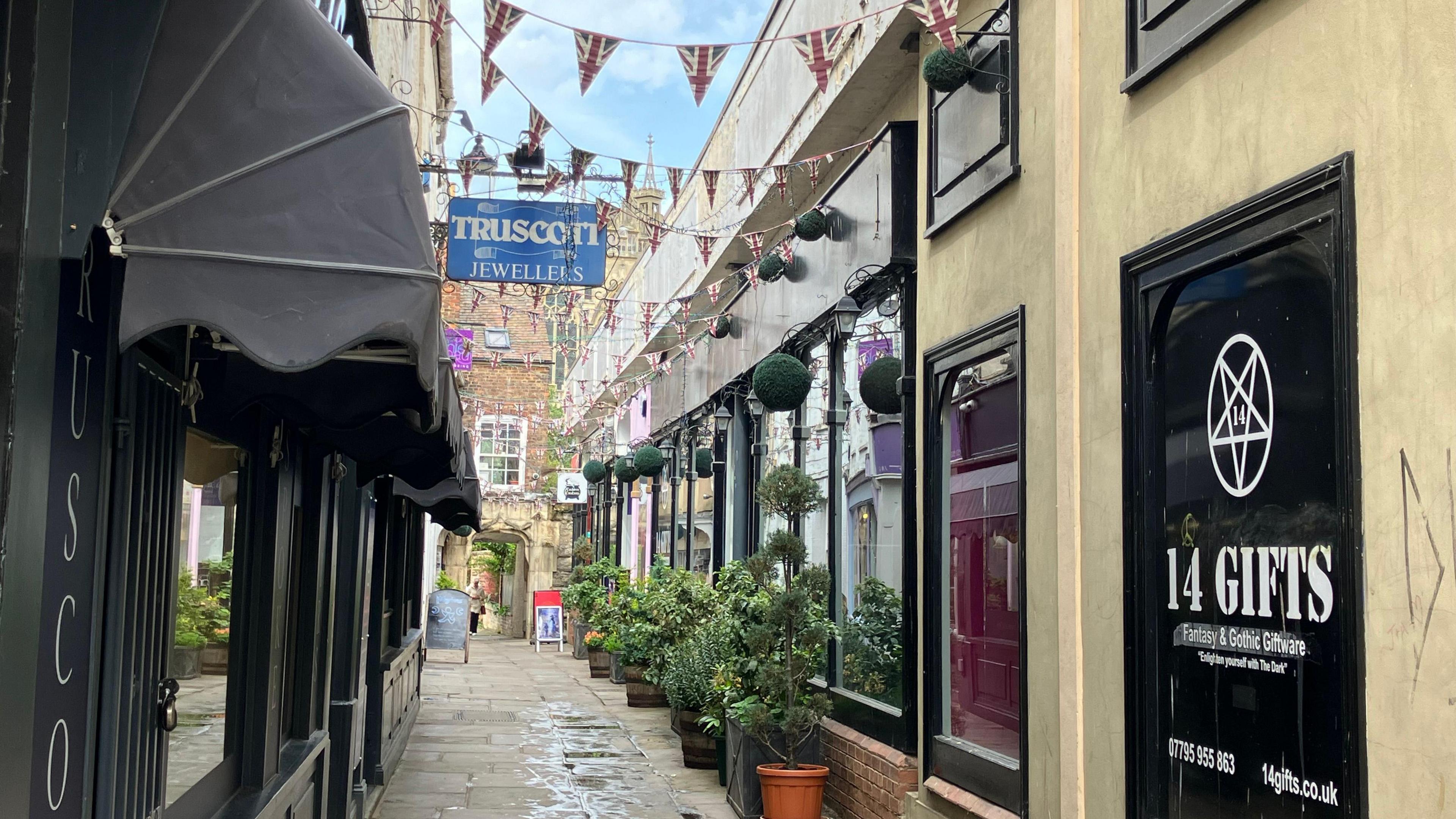 A photo showing a street in Gloucester with shops on either side and bunting stretching across from the buildings. In the background is Gloucester Cathedral