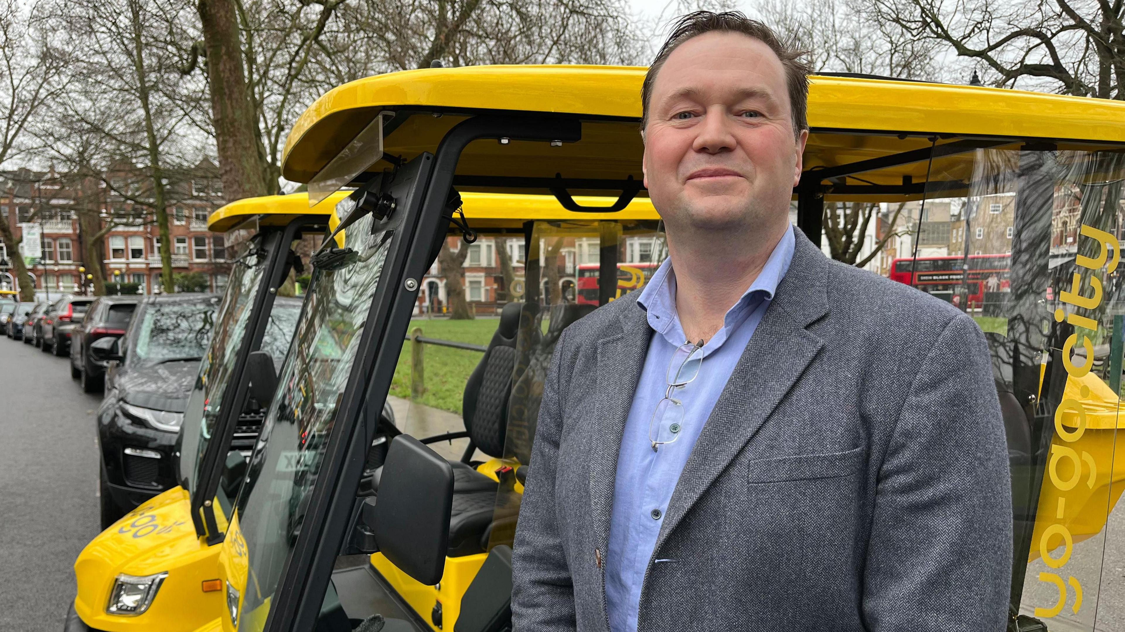 A man in a suit stands in front of a yellow buggy