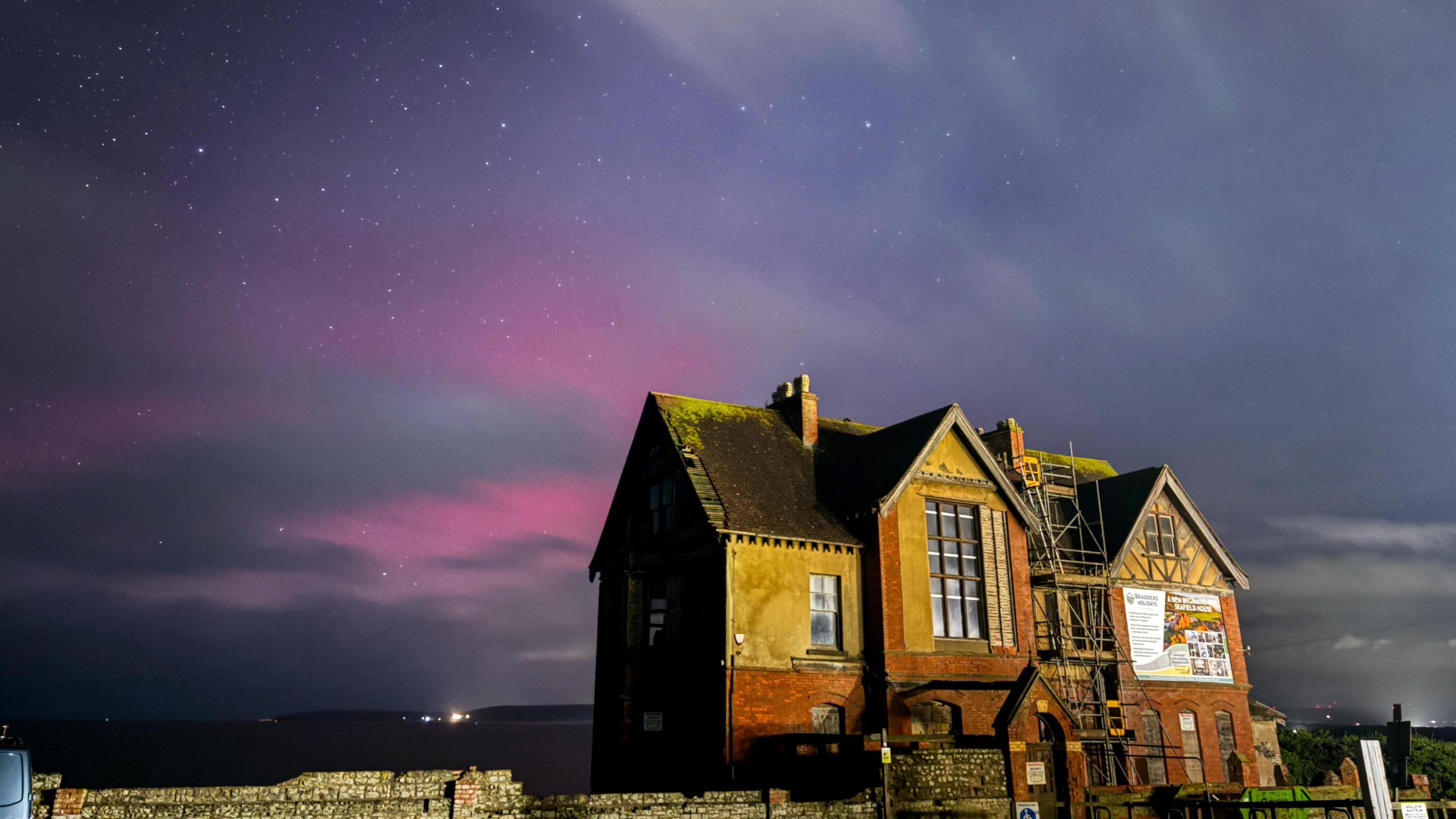 Northern Lights shine above an old house in Westward Ho!, Devon. The lights are purple and pink.