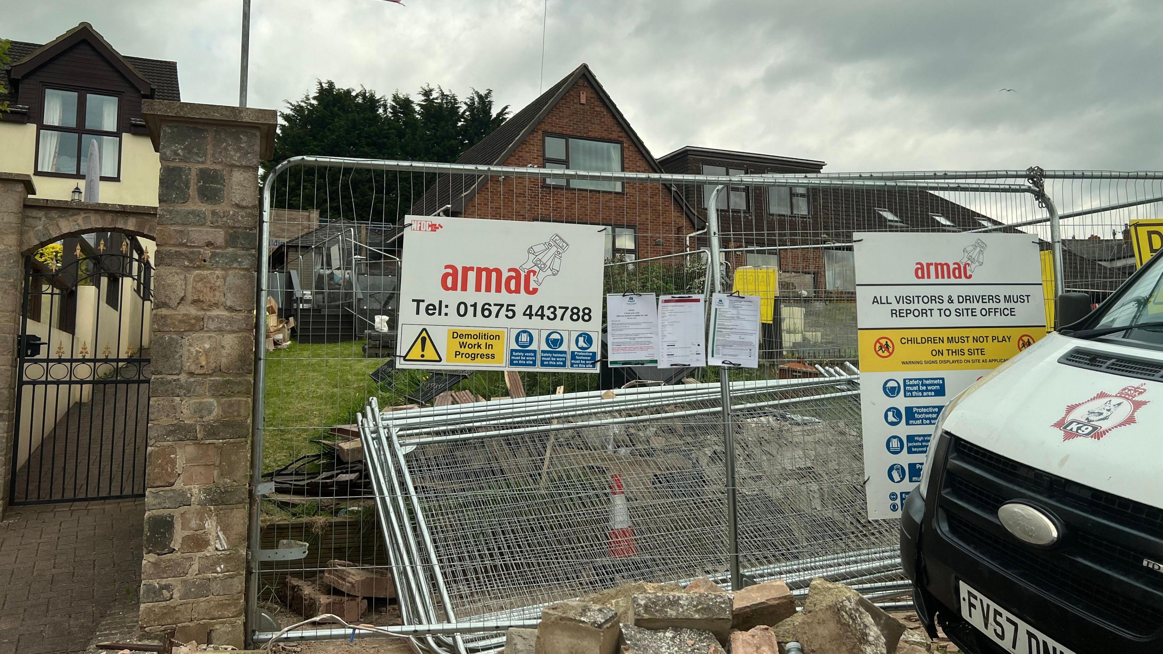 The fenced off property, with a sign on the fence saying "demolition work in progress". 