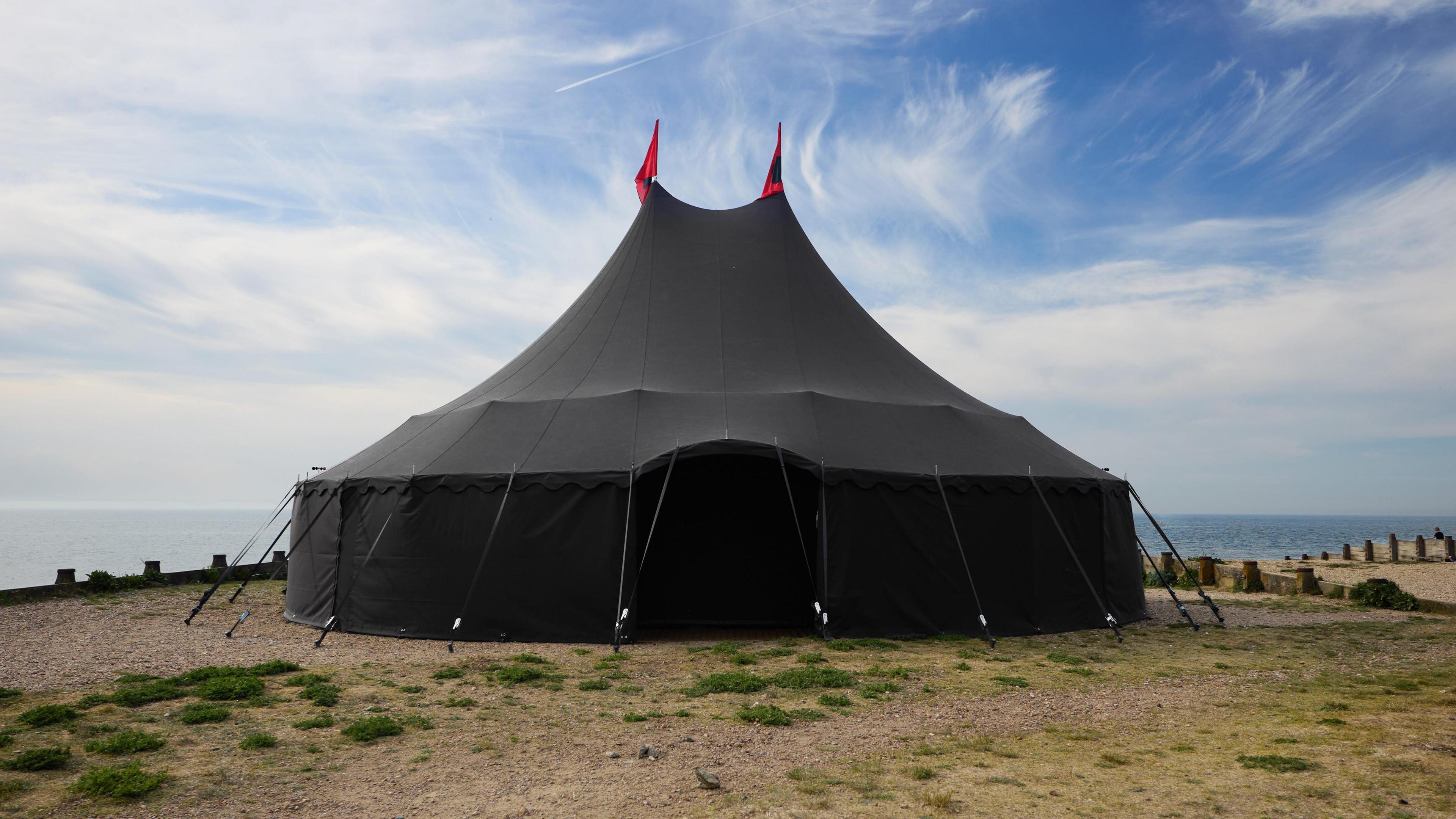 A large black tent which has been set up on a seafront.