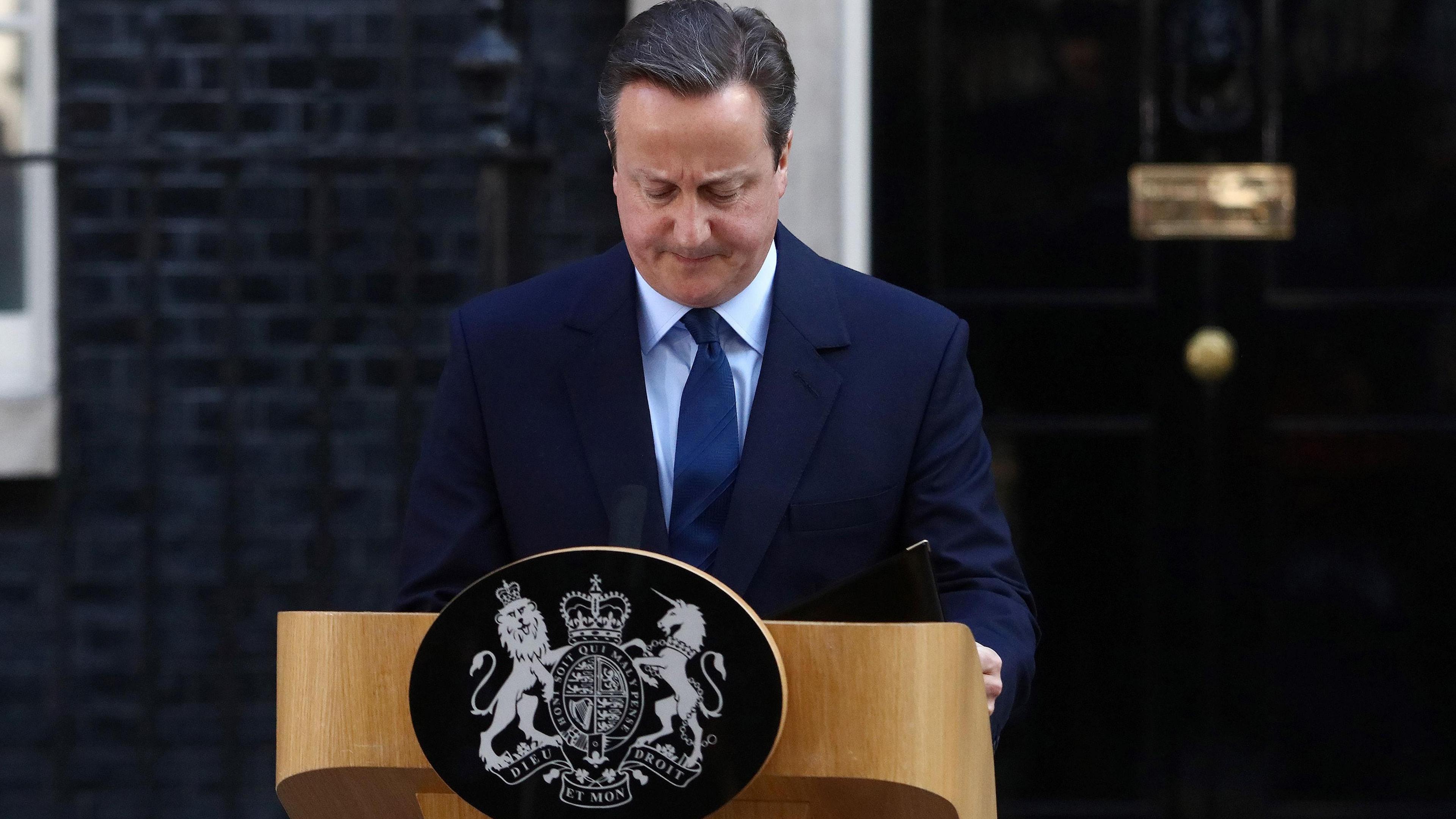 David Cameron is standing in front of a podium that's been put up outside Number 10 Downing Street. He's wearing a navy suit and looking down.