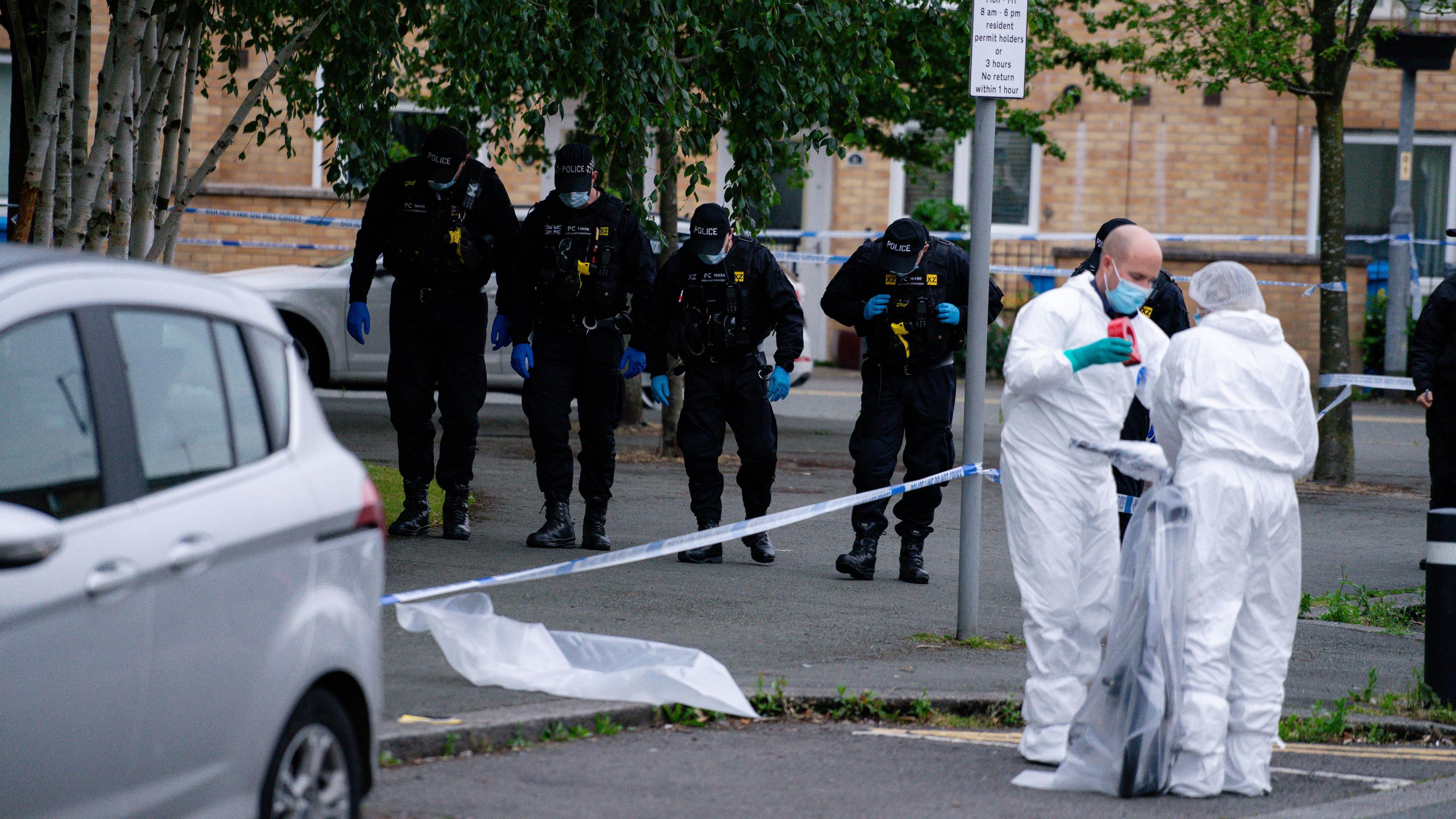 Four police officers conduct a search while two white-suited forensic investigators wrap a bicycle in plastic