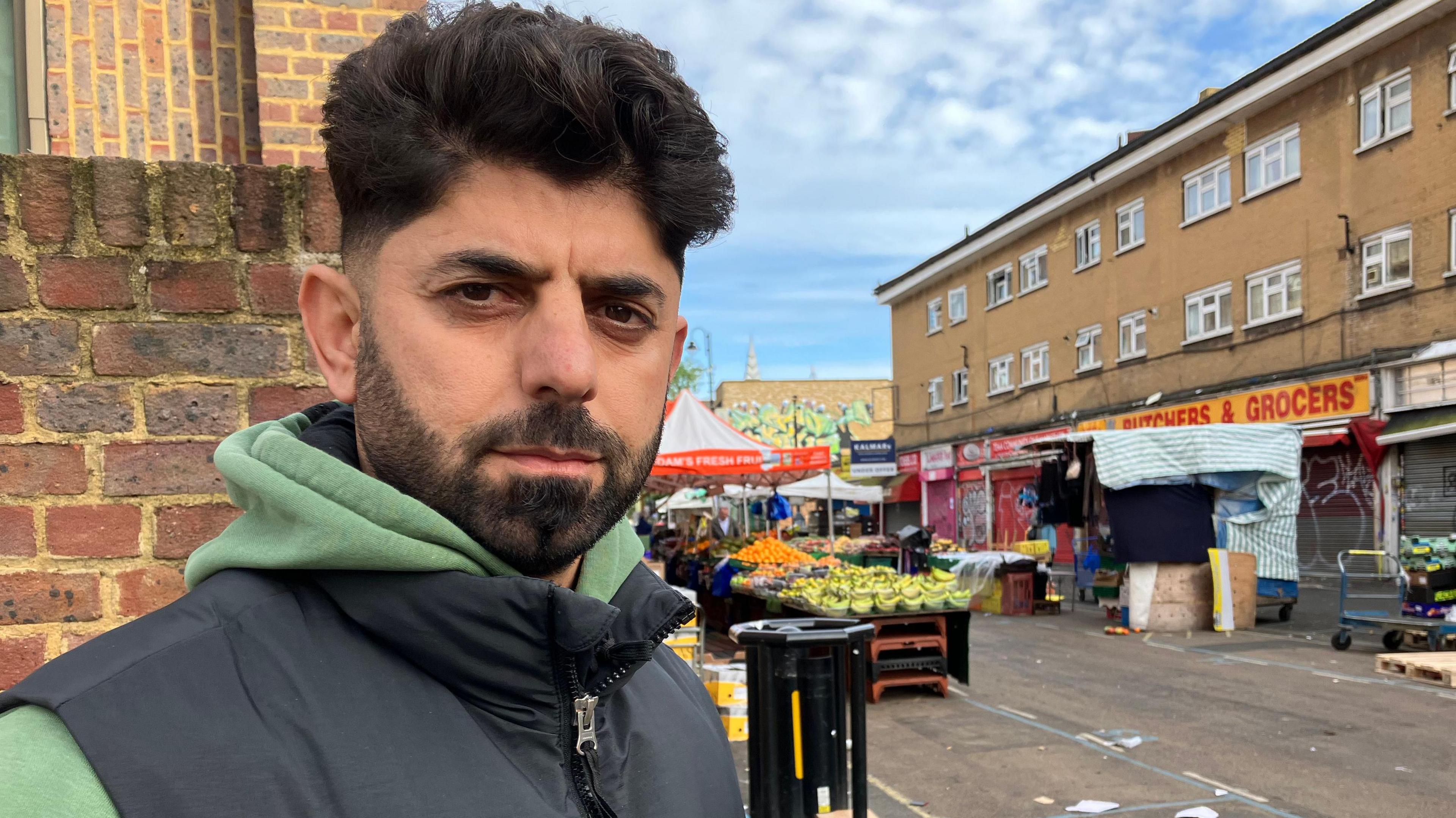 Adam Kadirzadah in a green hoodie and black gilet. He has dark hair and a beard and moustache. 