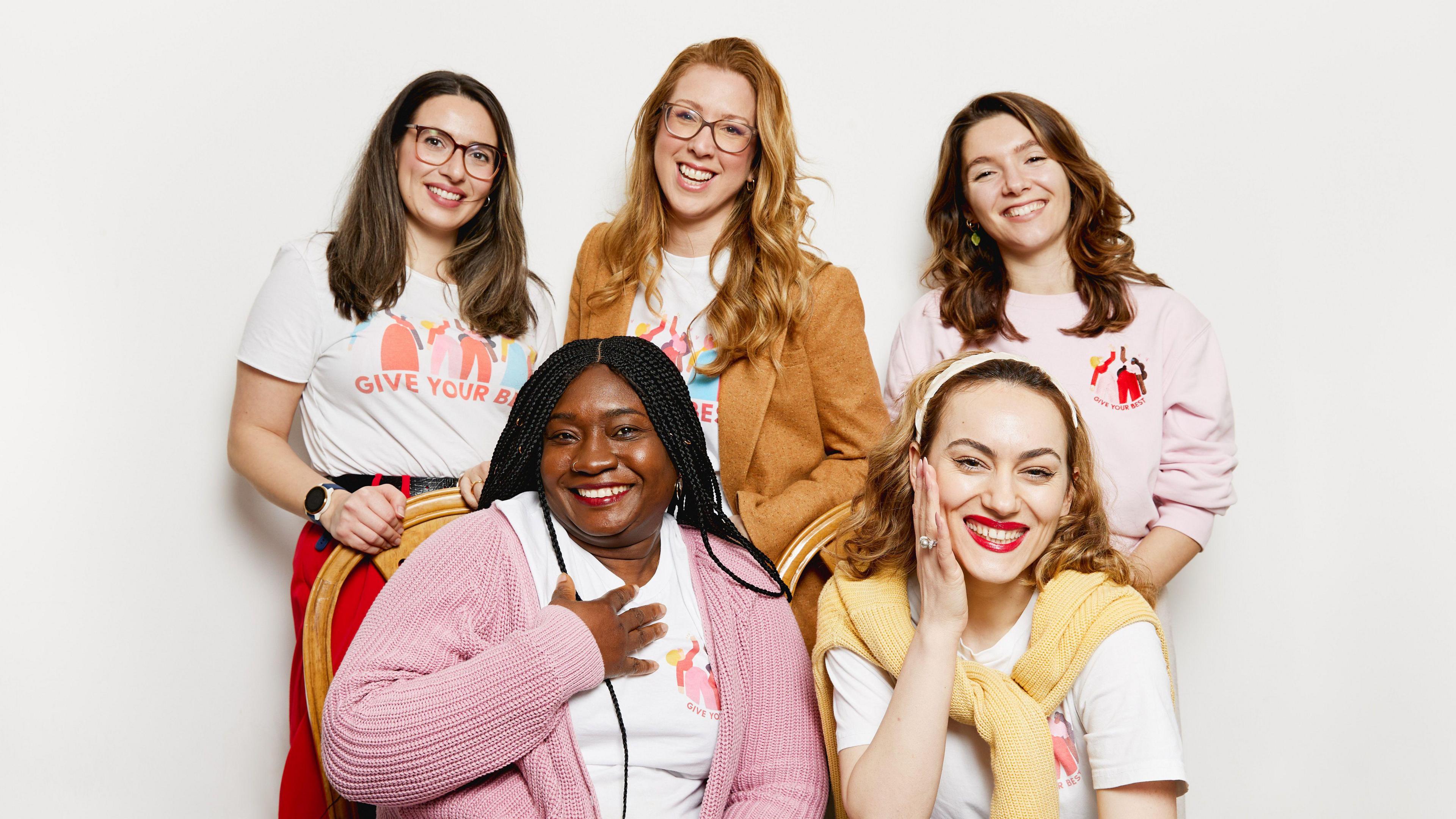 The Give Your Best Team and stand and sit for a professional photo wearing white t-shirts and pink and yellow sweatshirts with the company's logos. Left to right (top): Giuliana, Sol, Georgia. Bottom: ambassadors Kemi, Sidorela