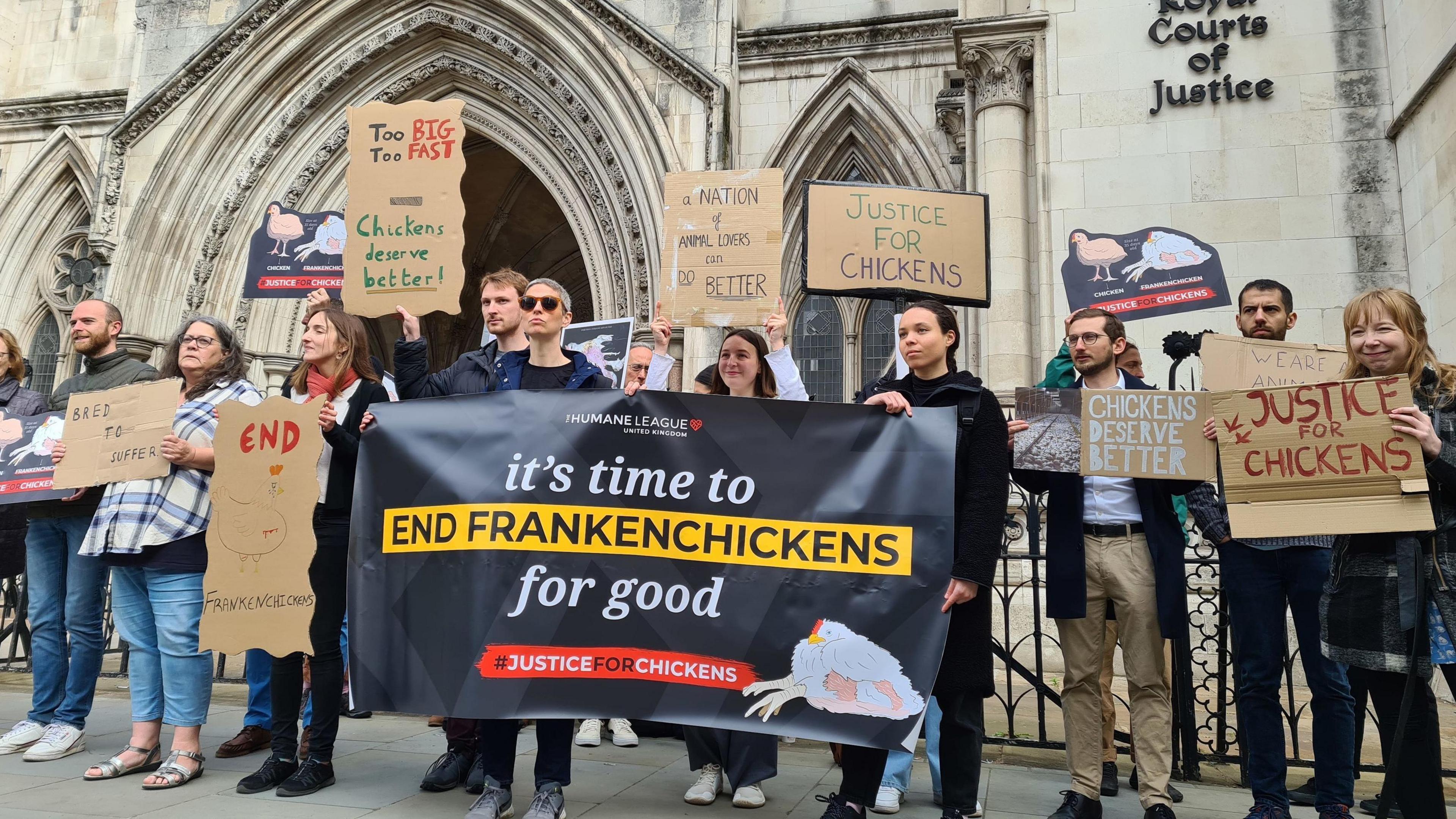 Campaigners stand outside of the Royal Court of Justice in London holding banners. One reads "it's time to end Frankenchickens for good".