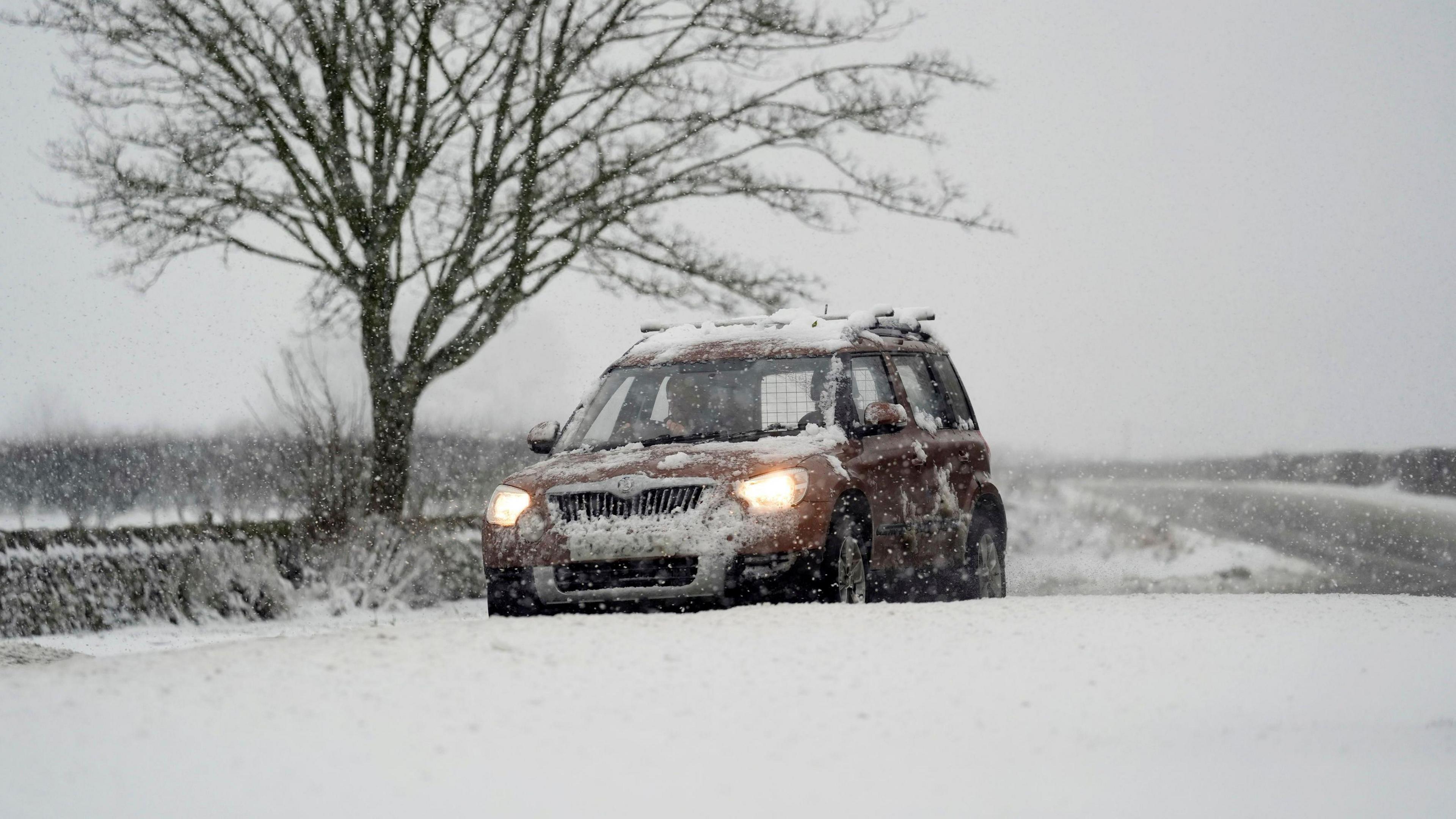 A car drives through snow on the A169 between Pickering and Whitby on the North York Moors