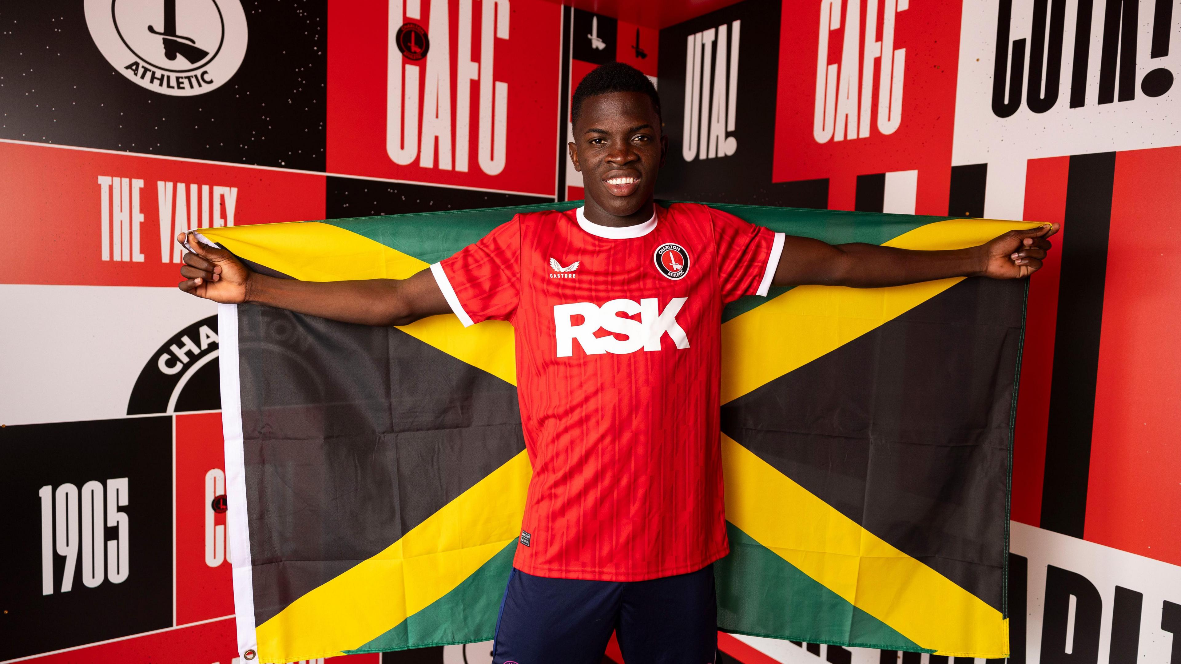 Kaheim Dixon poses with a Jamaica flag, wearing a Charlton Athletic shirt