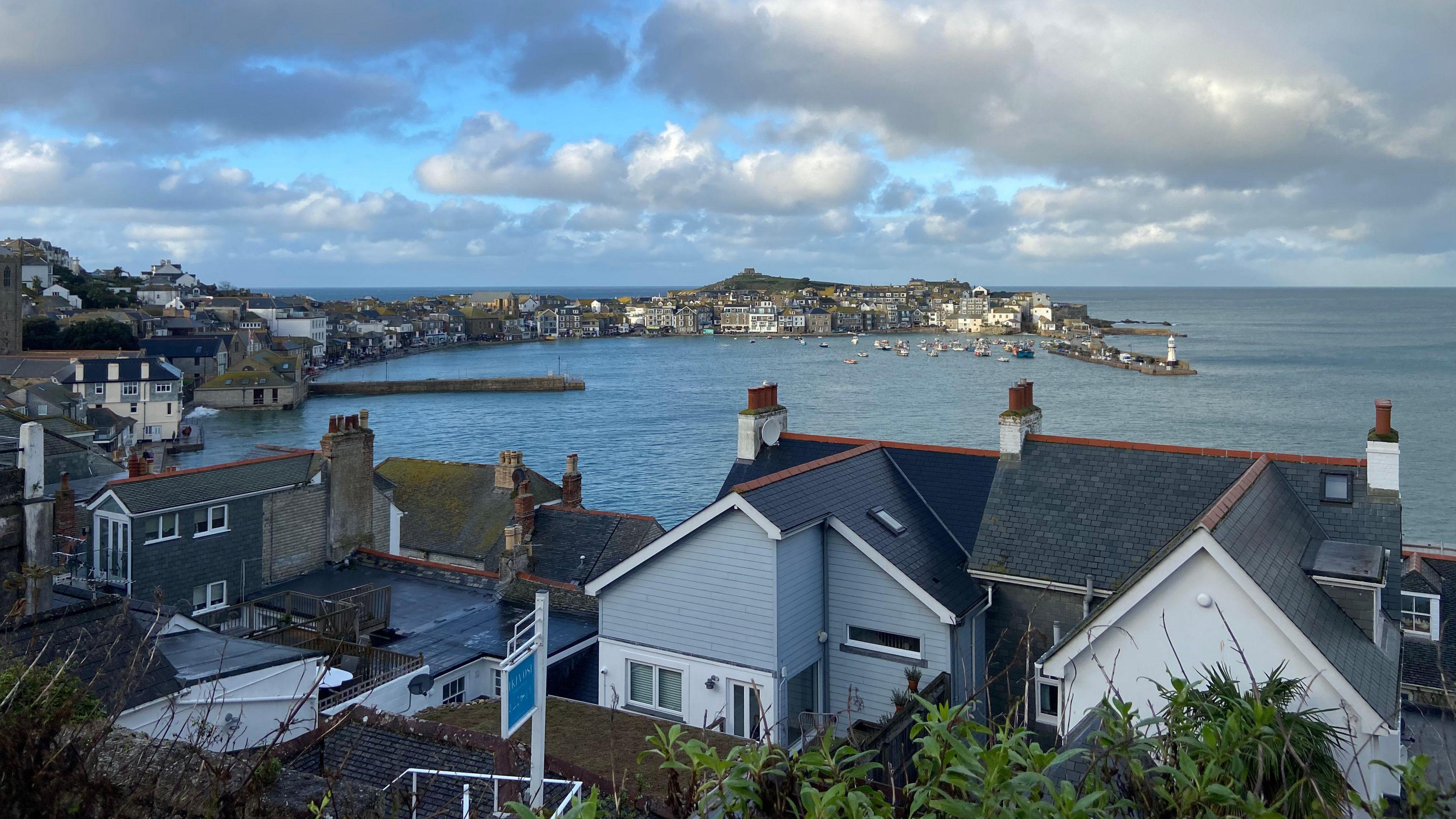 General view of St Ives in Cornwall. The image is taken from above a group of houses that overlook the sea on a sunny but cloudy day.