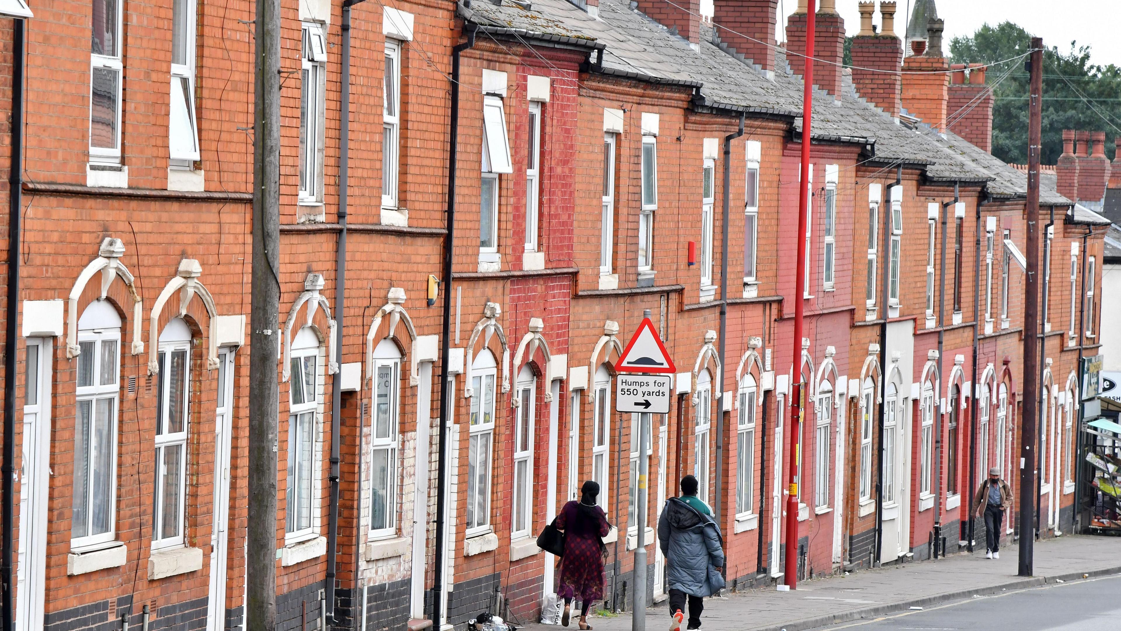 A row of red terraced houses, two women walking down the street