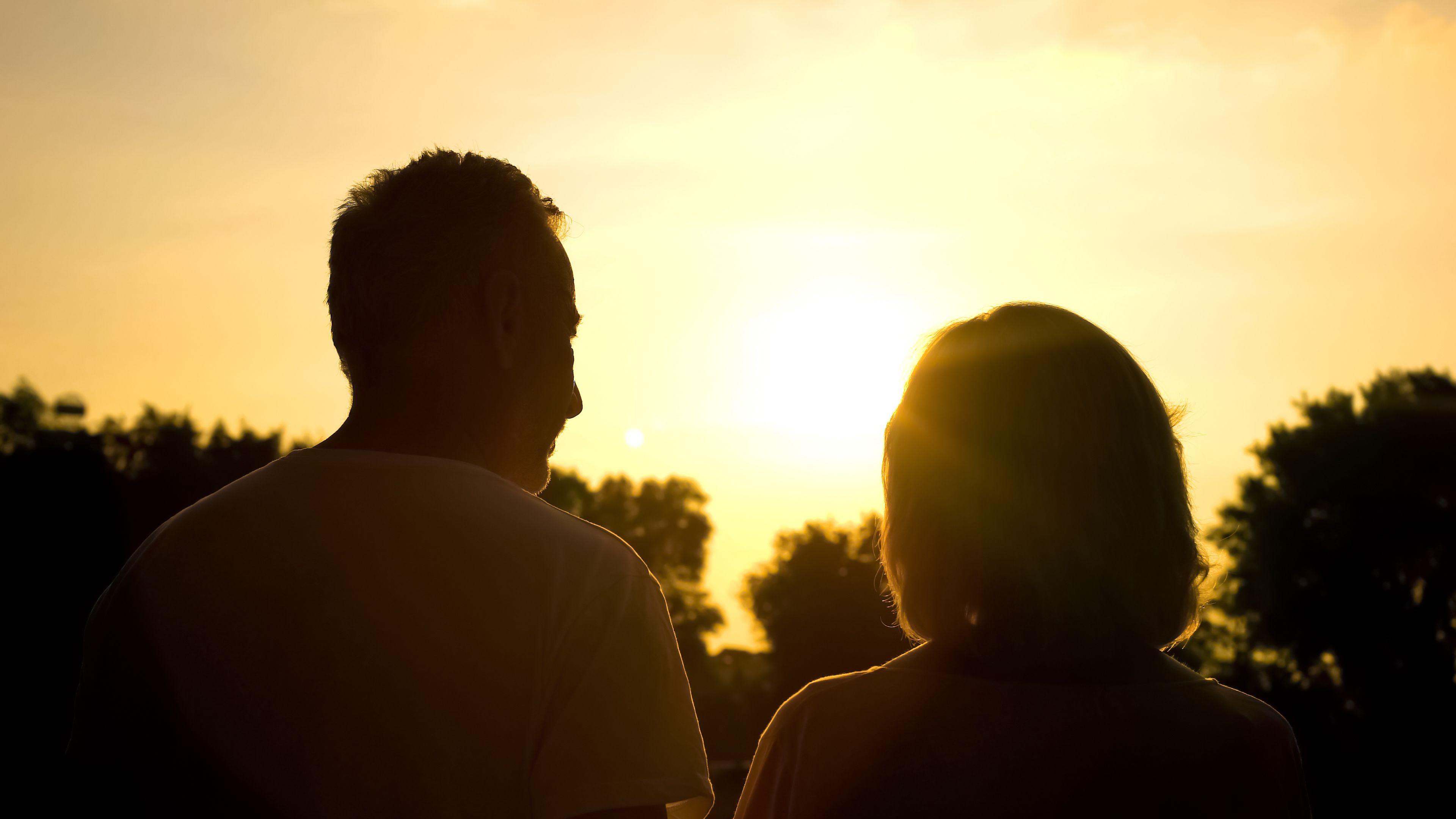 A couple pictured from behind, outside at sunset and in silhouette.