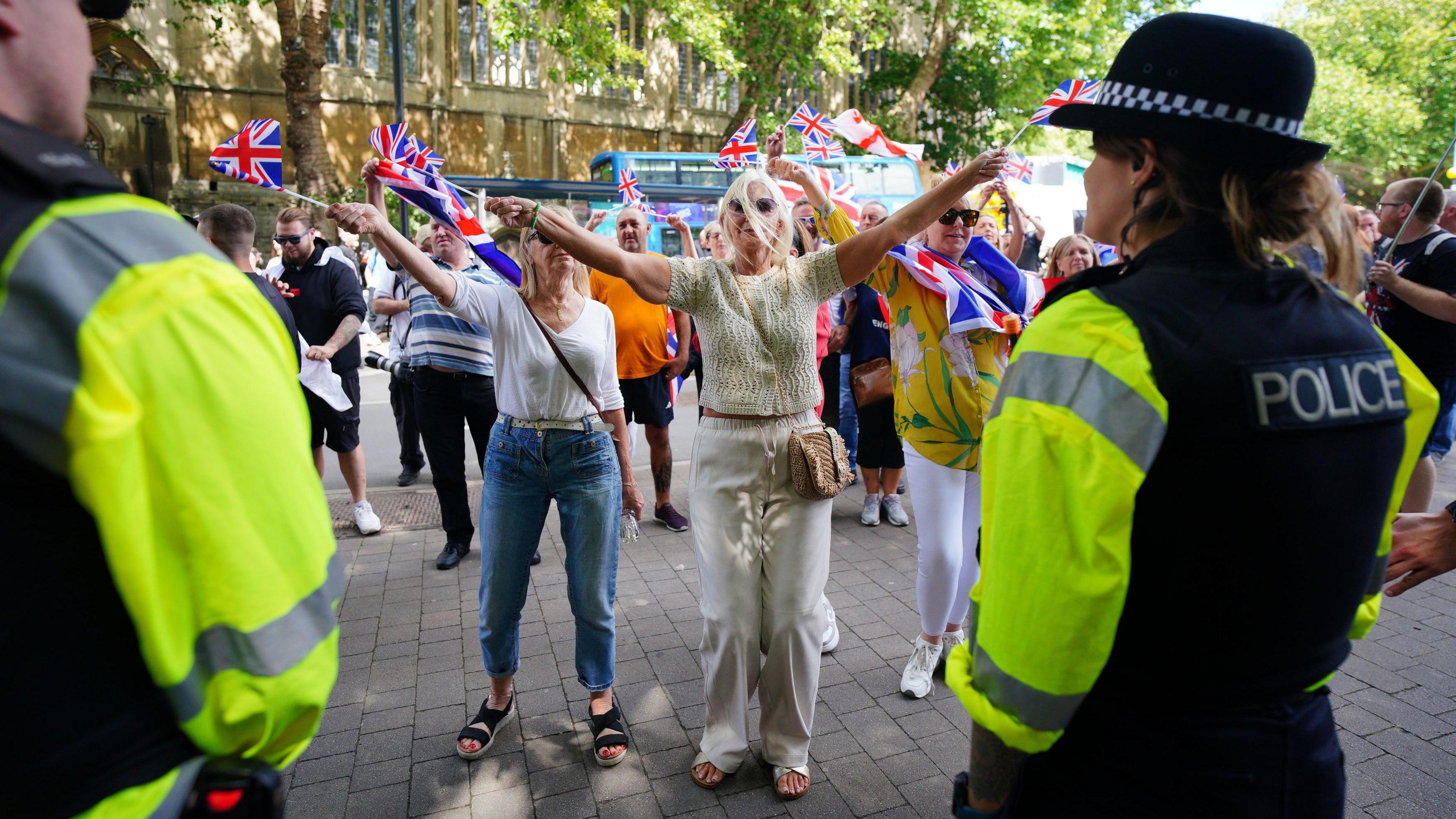 A group of anti-immigration protesters waving Union flags walk down a Bristol city centre street as police, with their backs to the camera, watch on