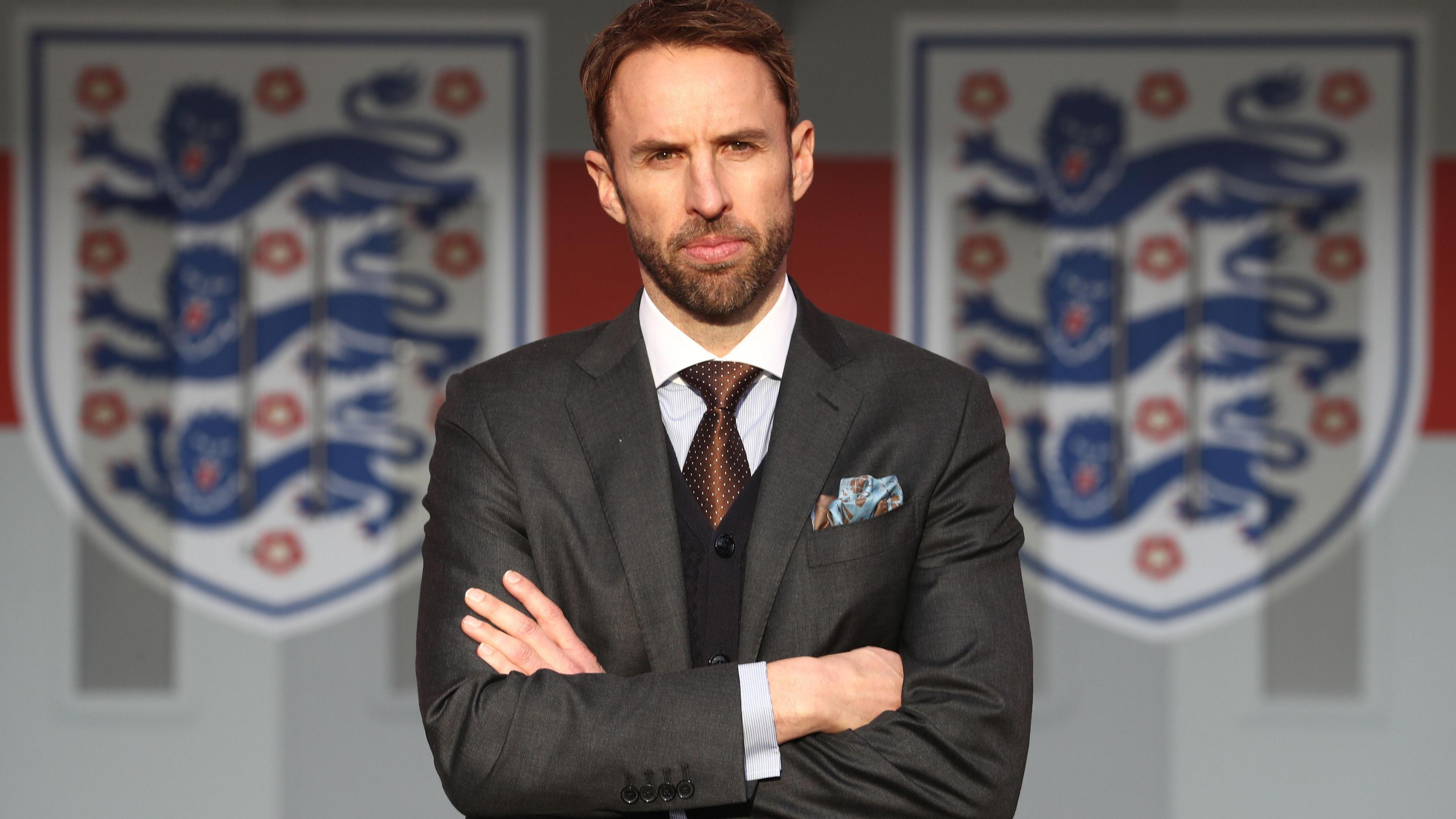 Gareth Southgate stands in front of two England crest