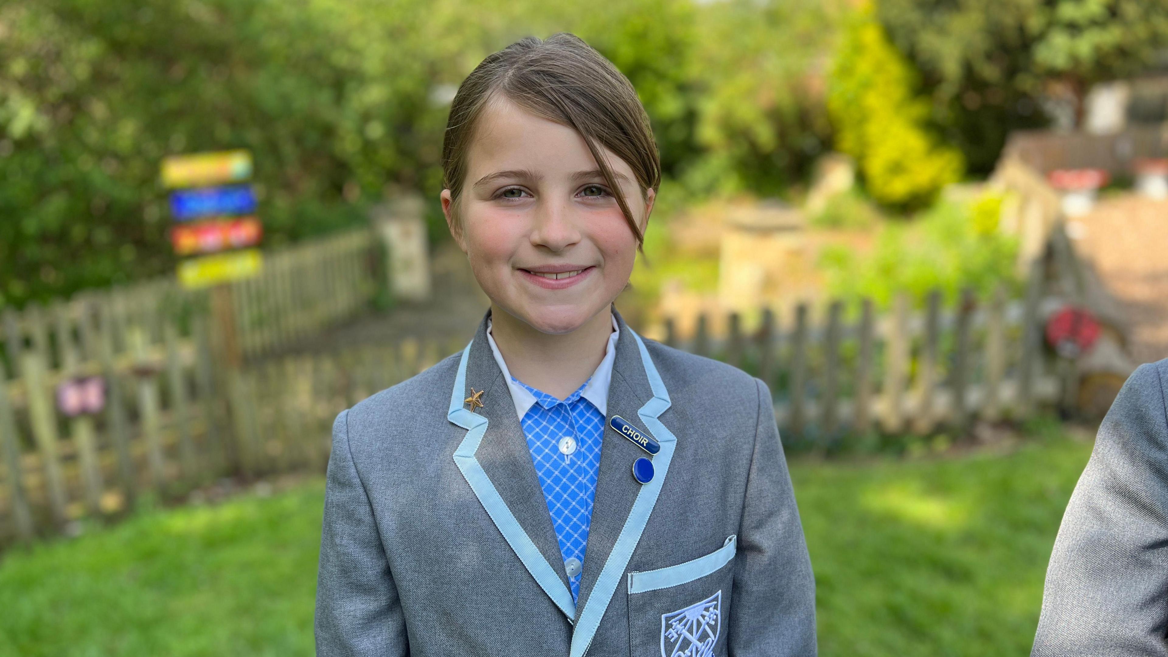 Persephone - girl with dark hair tied back wearing grey uniform