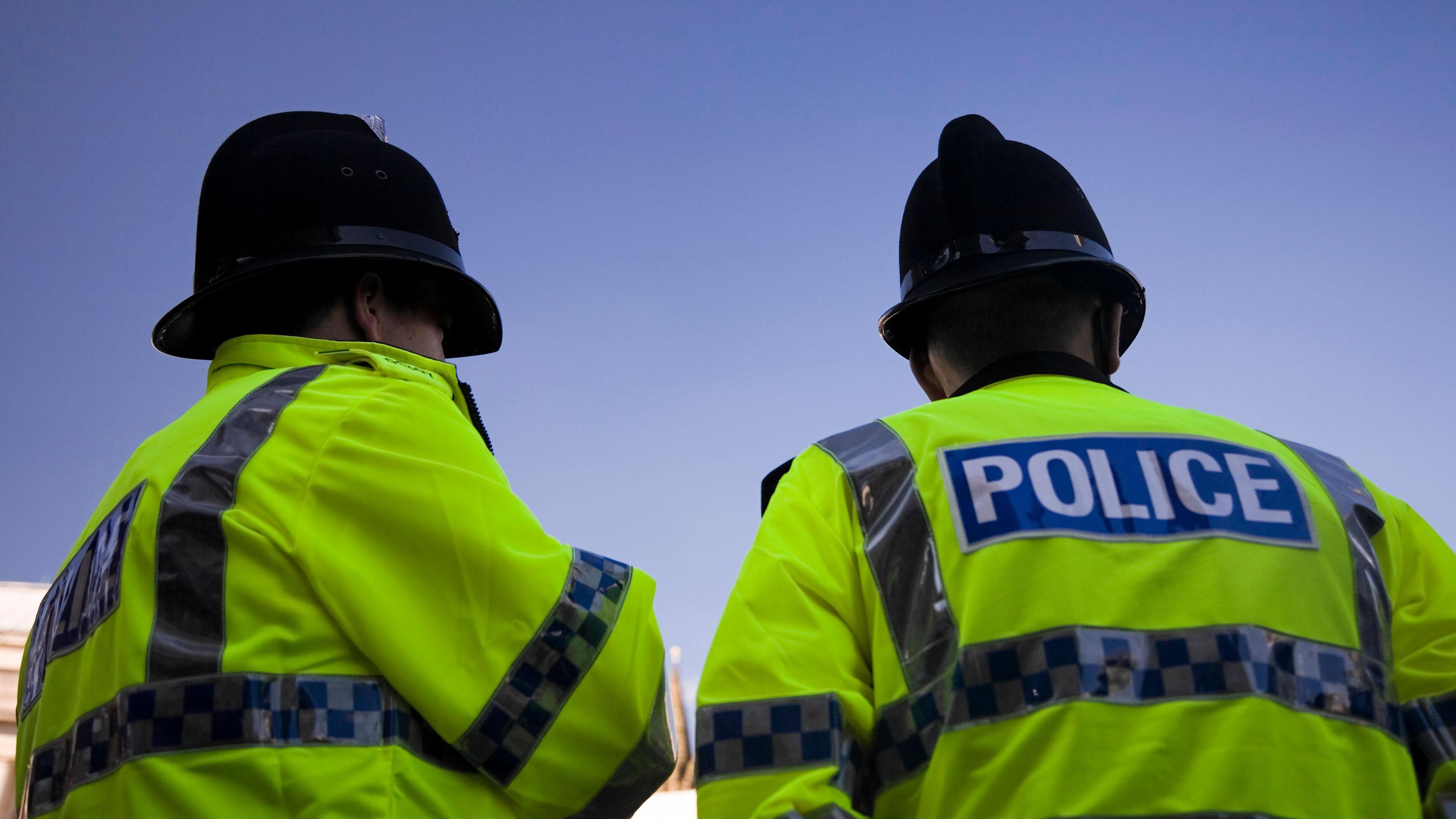 Two police officers in high vis jackets and helmets facing away from the camera