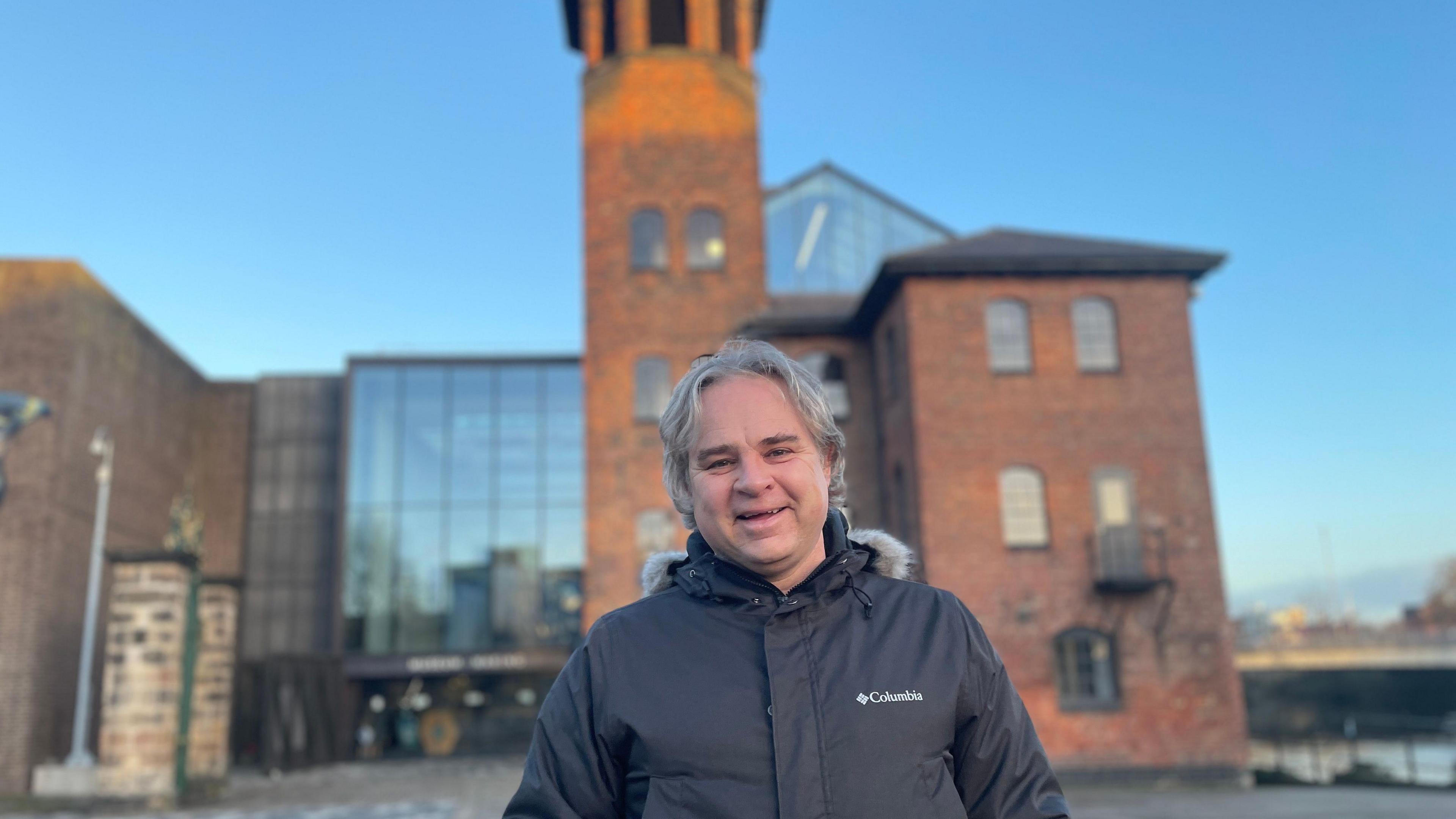 A man with grey hair and wearing a coat stood outside the museum of making in Derby city centre