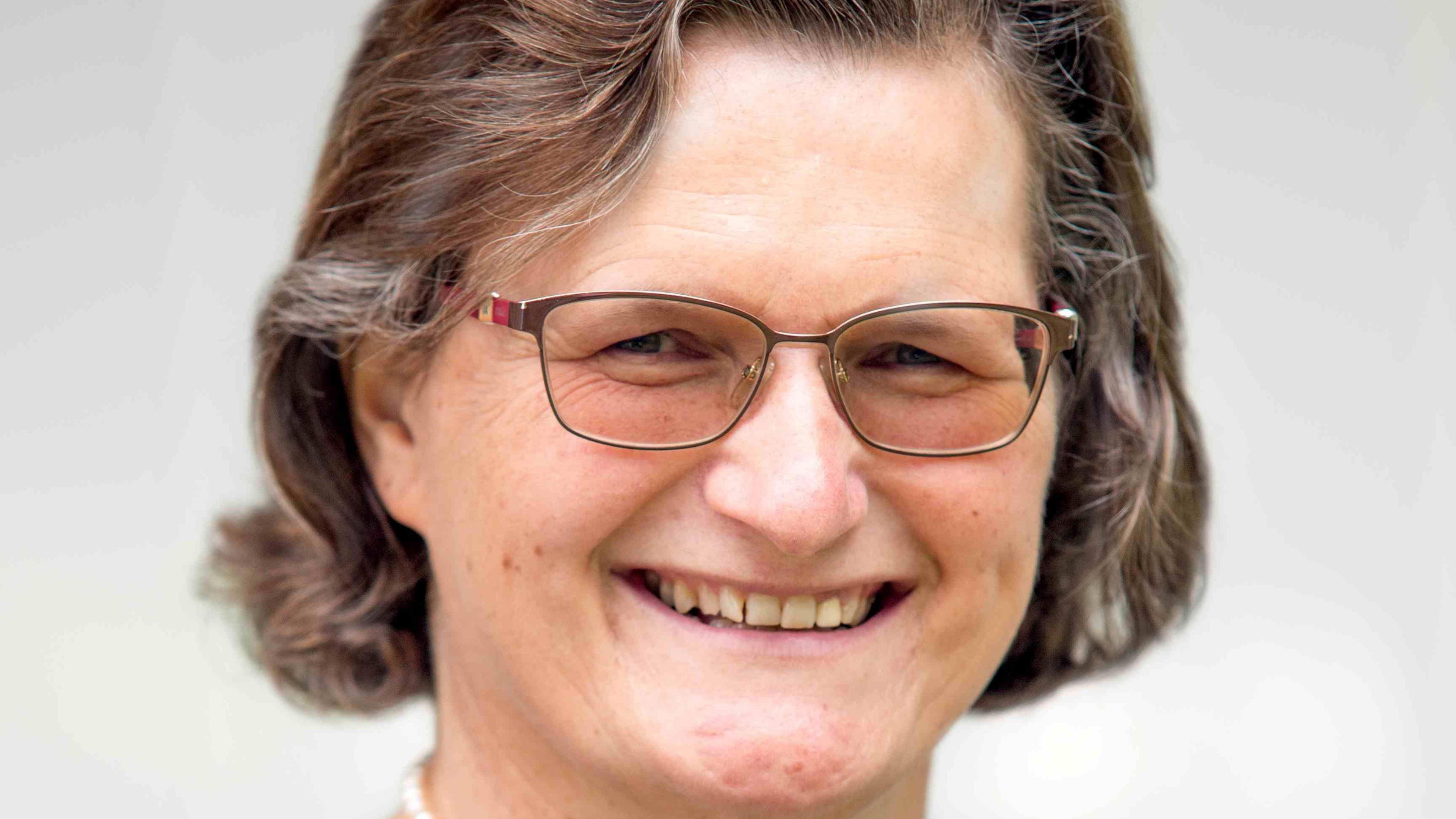 A smiling woman in glasses with a brown curly bob.