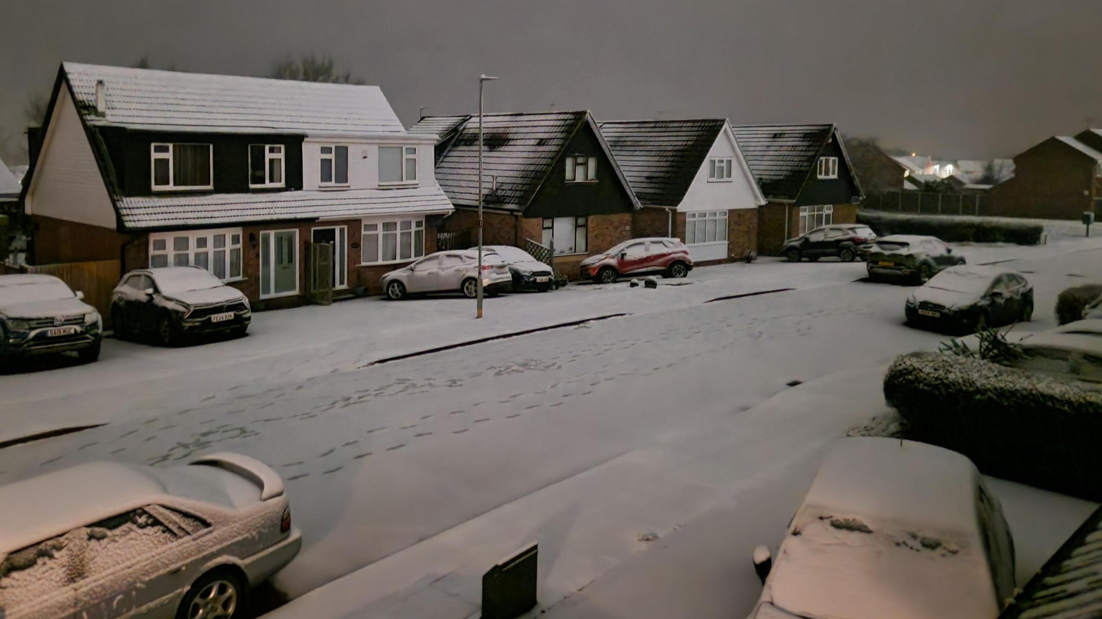 Snow covering a street and cars during the night