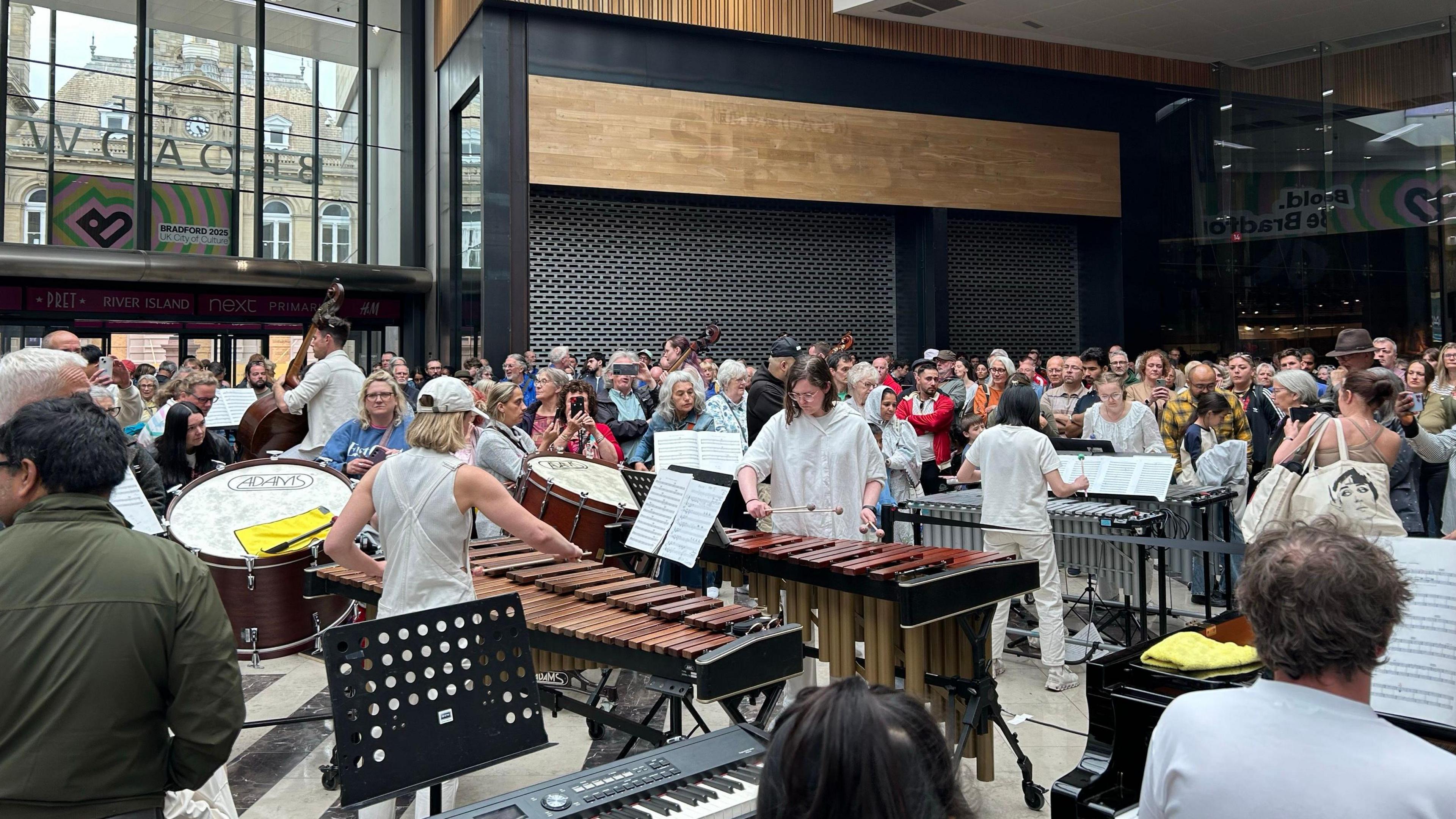 People playing instruments in the Broadway shopping centre with people watching.