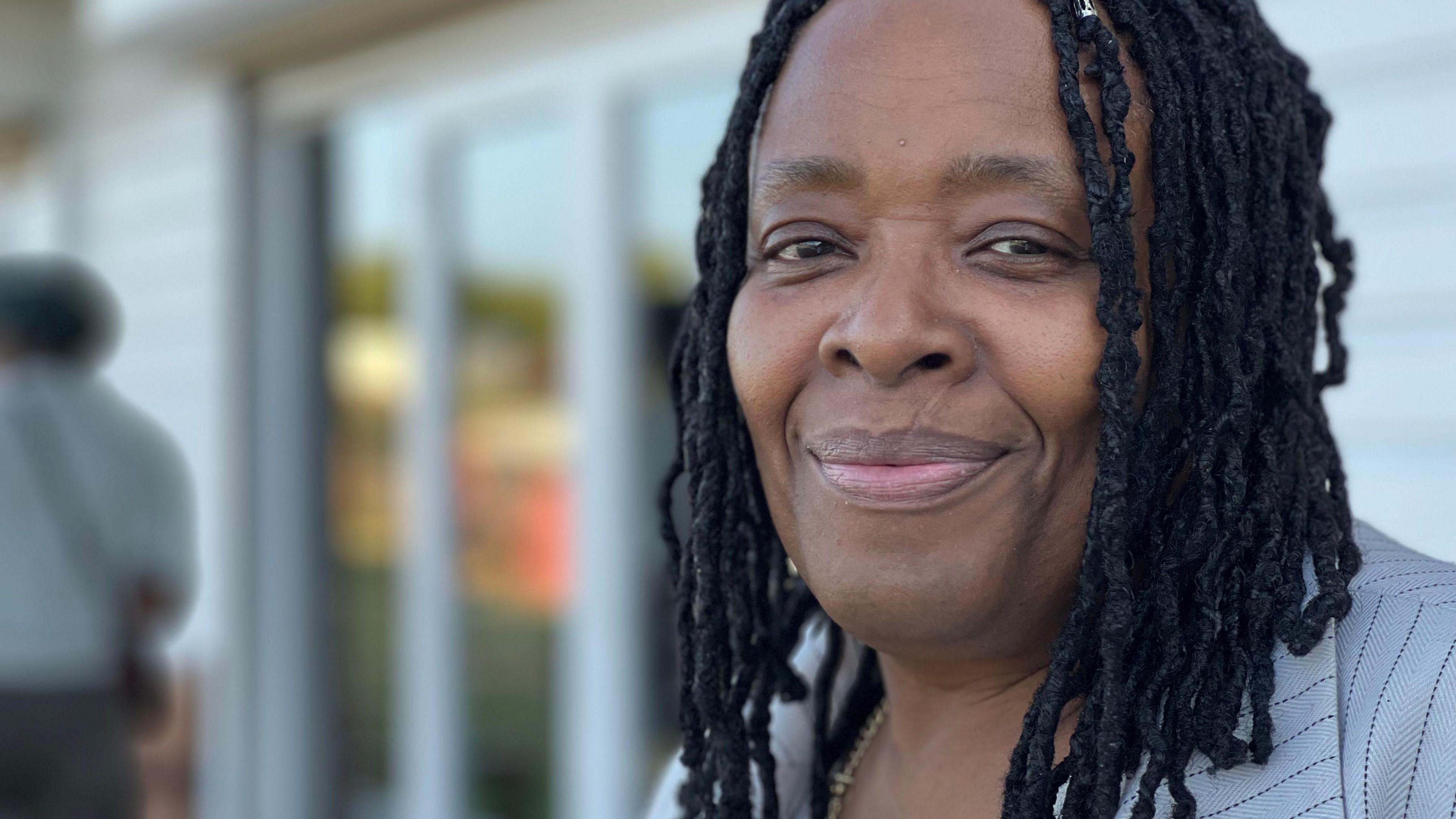 Jacqui Wilson smiles into the camera. She has black braids and is wearing a grey jacket.