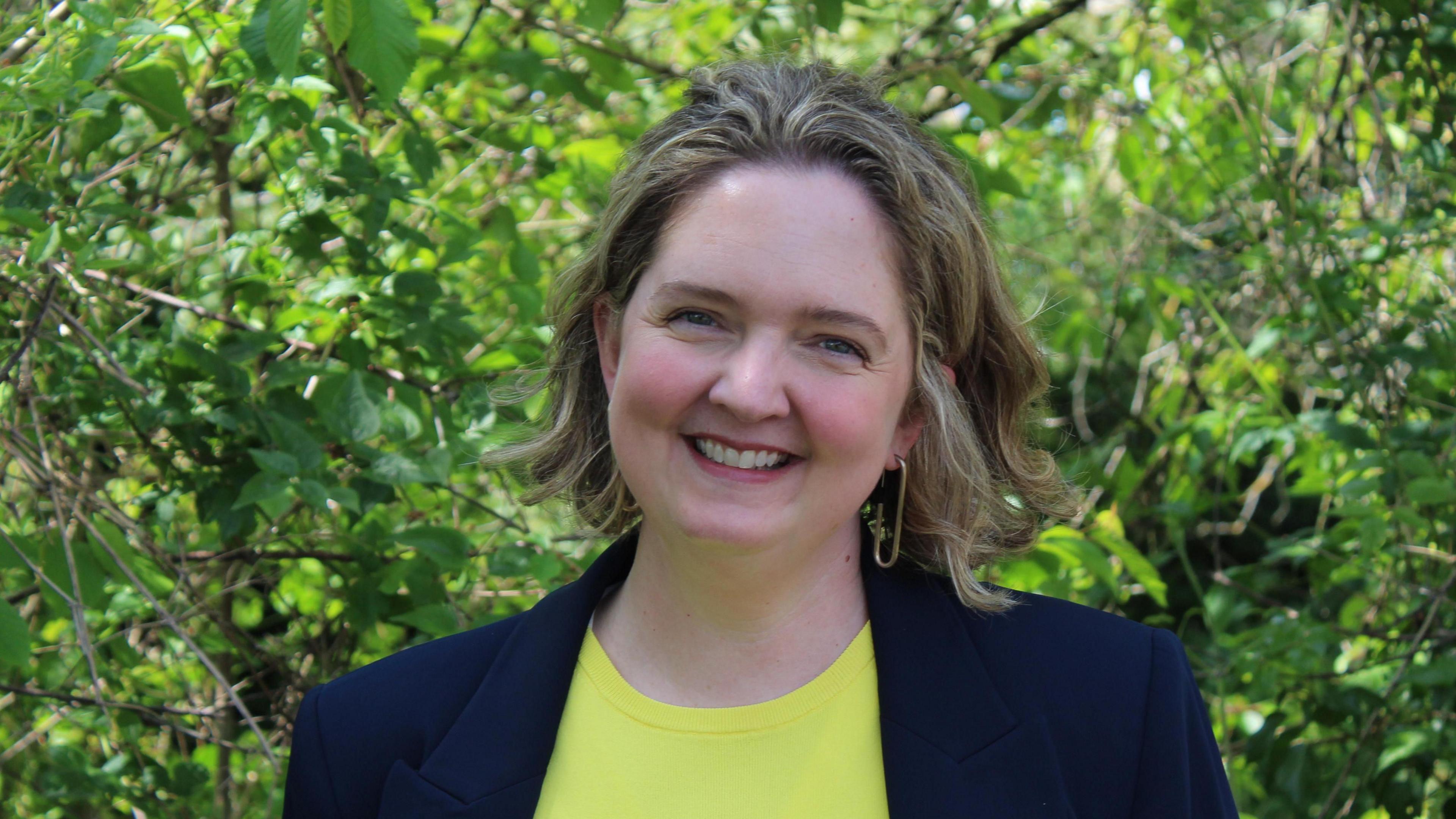 Anna Sabine in a yellow top and blue jacket in a garden.