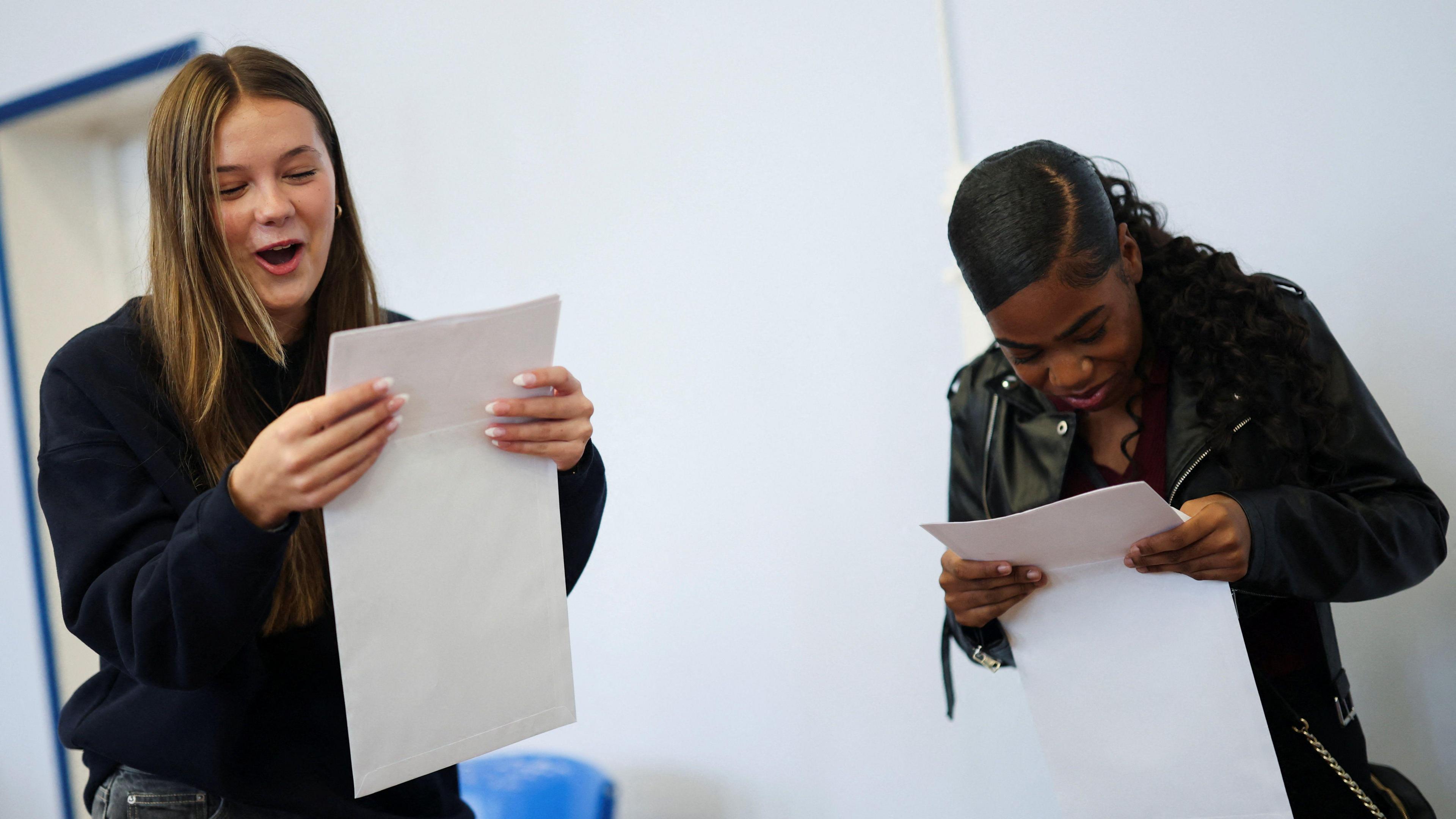 Two teenagers look at their pieces of paper with results on in shock and concentration