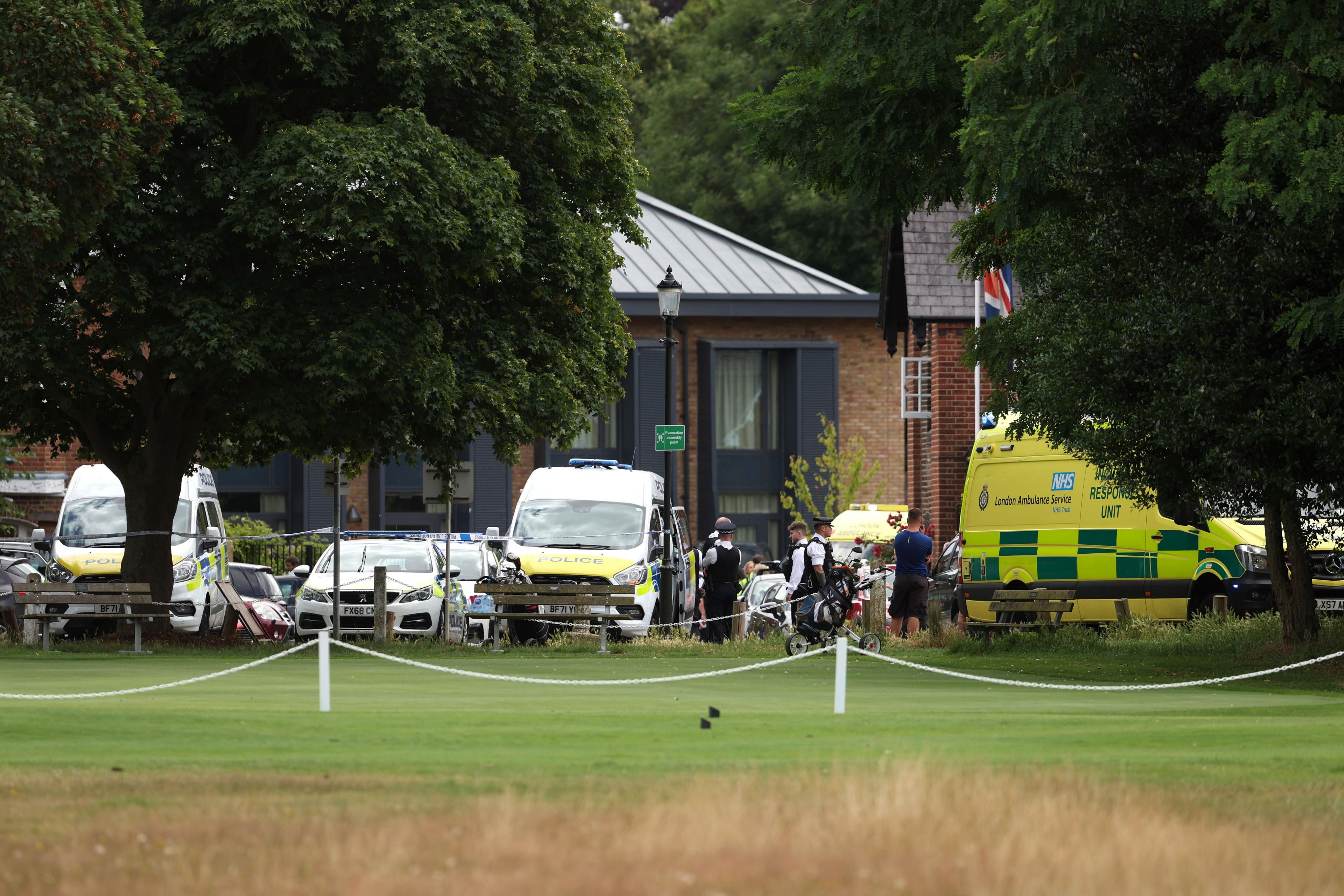 Across a green field, emergency vehicles and police at the scene of school between two trees