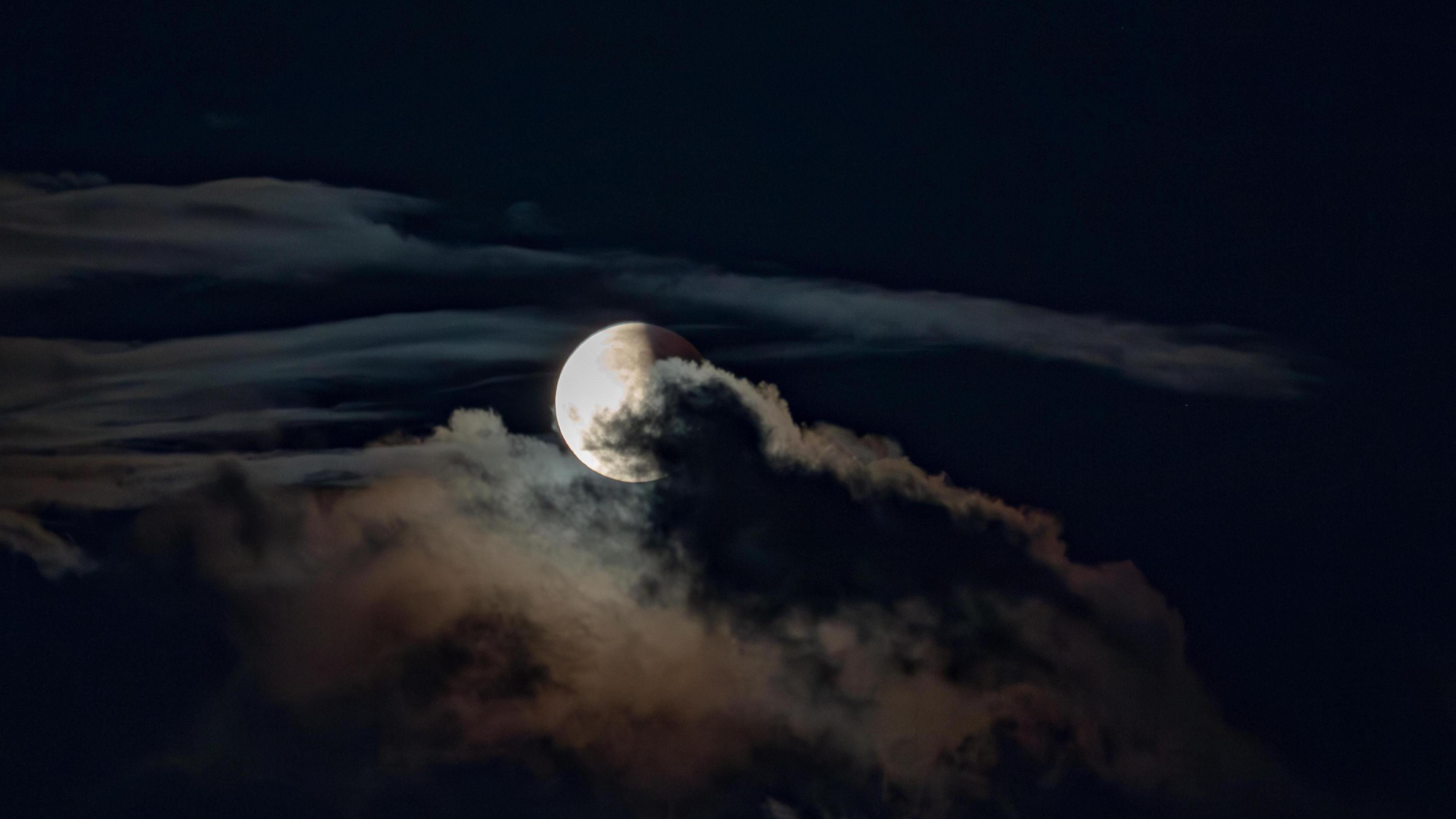 The is moon partially obscured behind clouds with a shadow over half of it. 