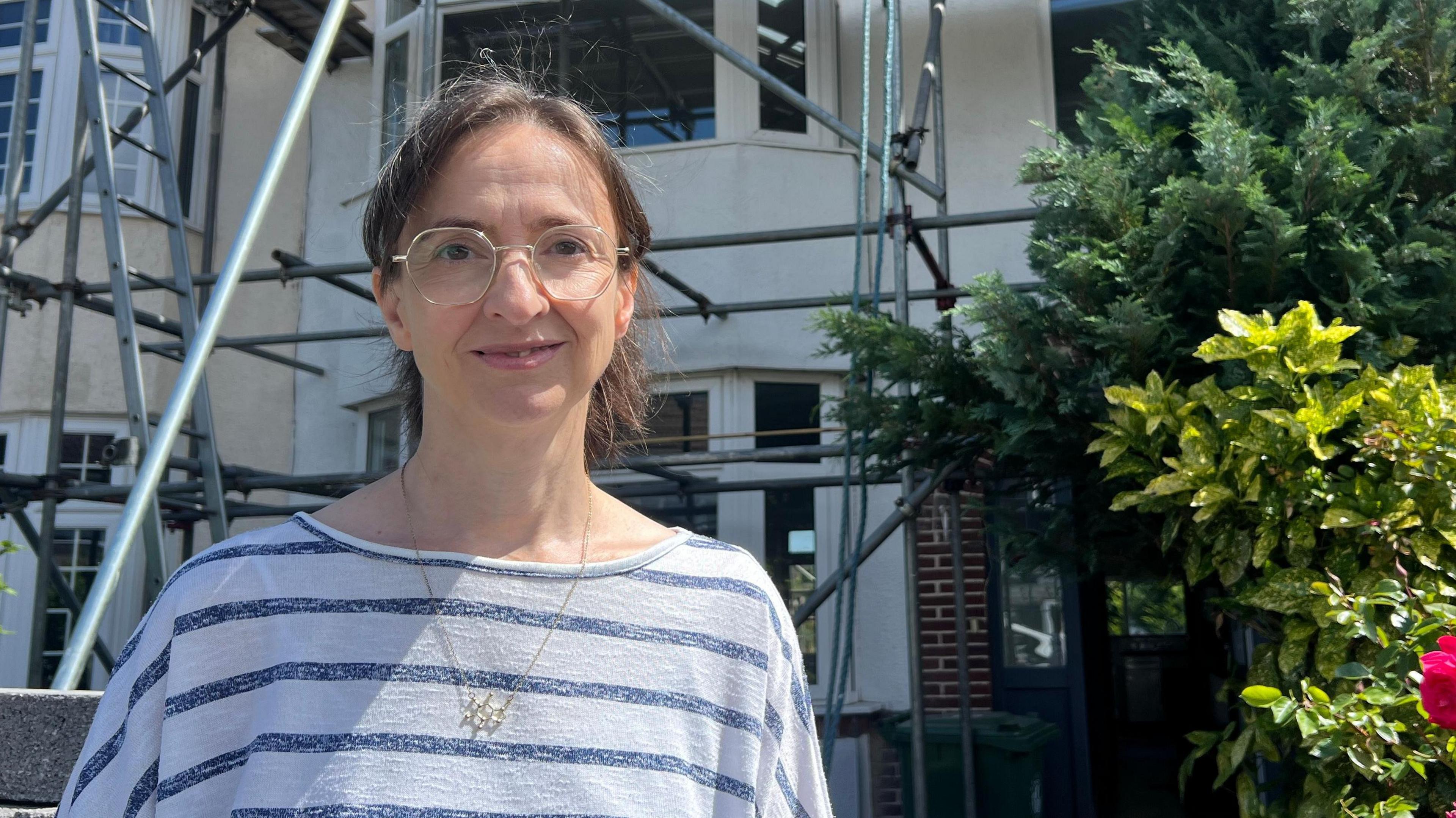 Jenni Sadler standing in front of the house she inherited - it is white and covered in scaffolding as work is ongoing to bring it back into use