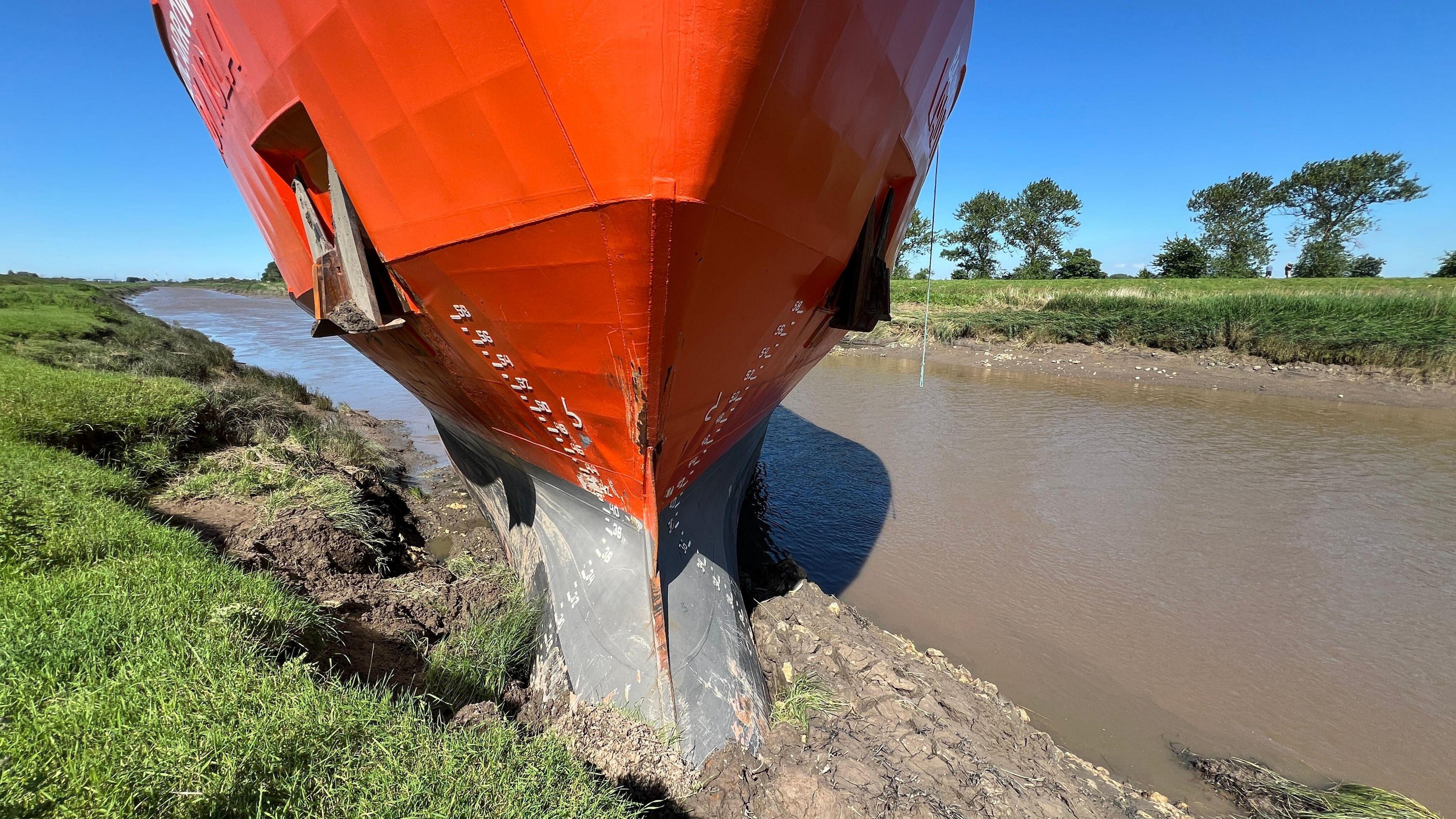 An orange cargo ship stuck in a river bank. 