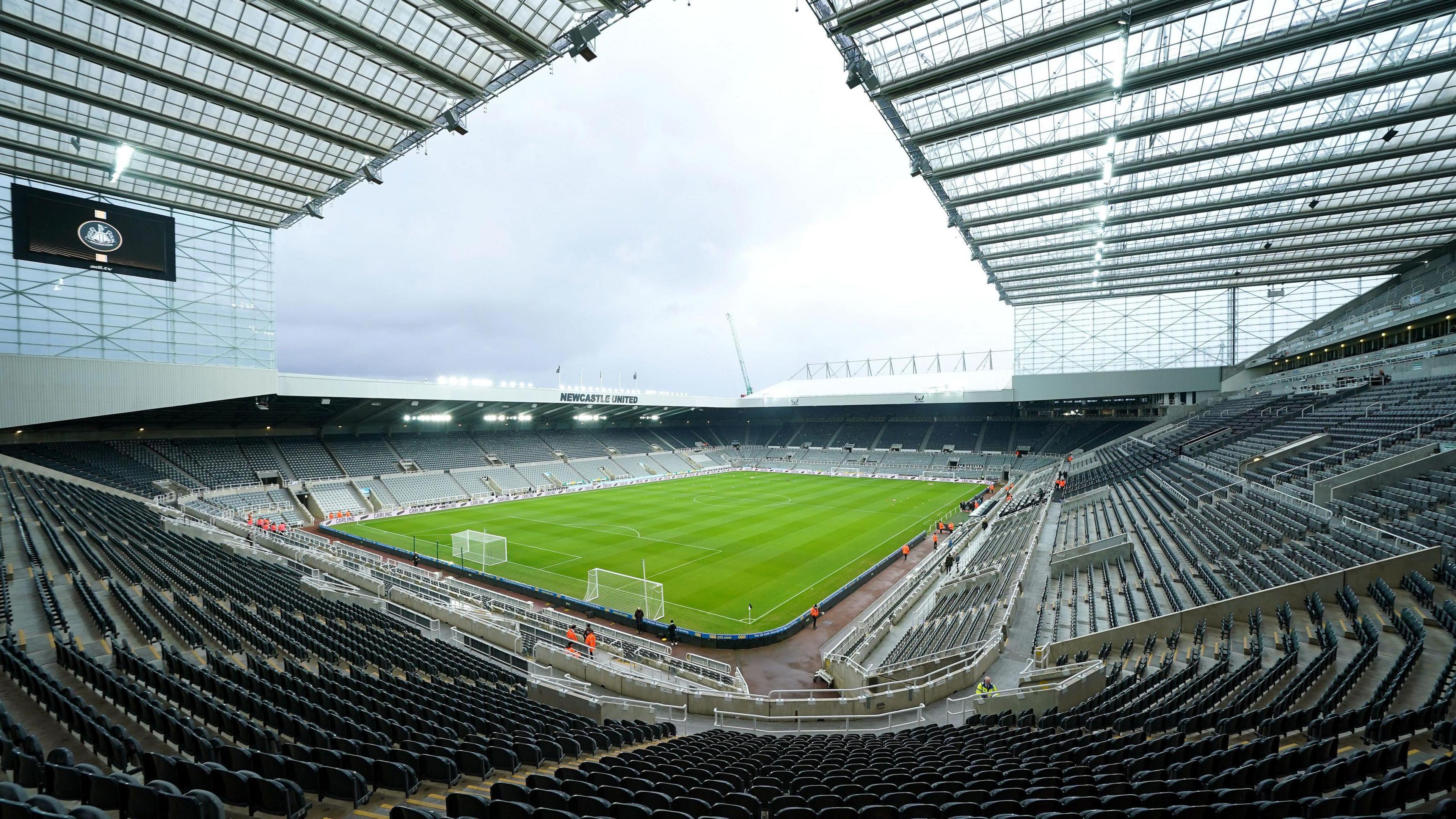 Inside St James' Park. It shows a lush green pitch. The stadium is empty. Newcastle United is written on the roof.