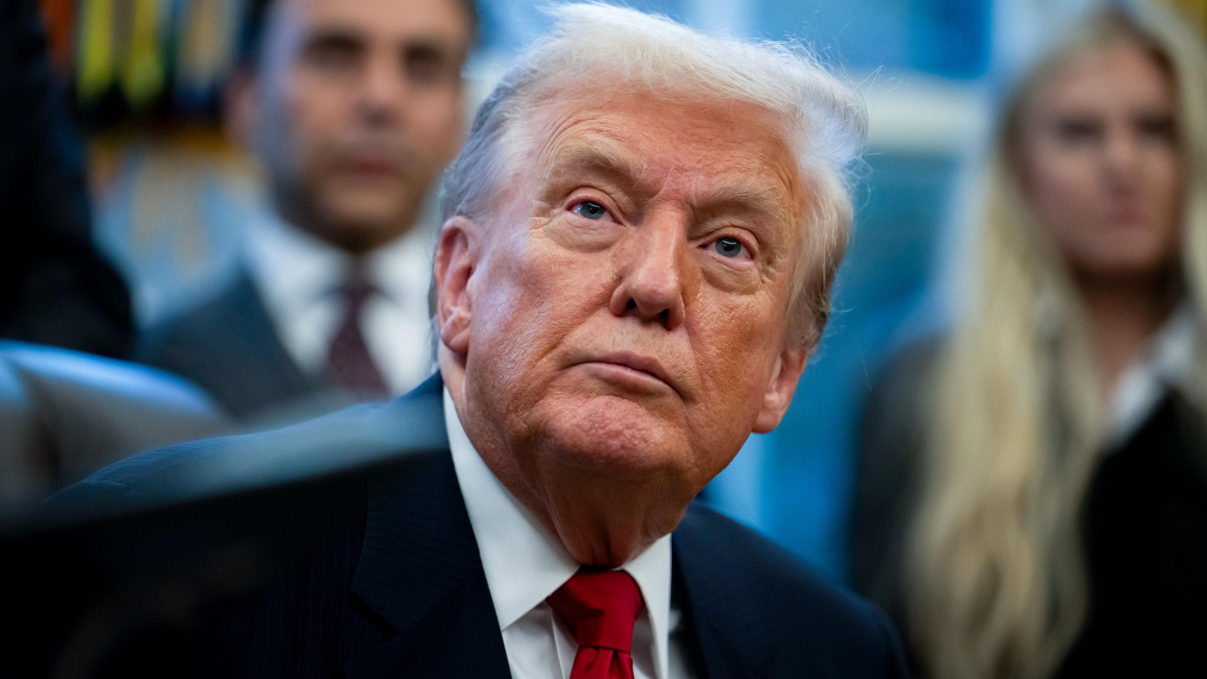 Donald Trump appears in a dark suit and red tie in the Oval Office