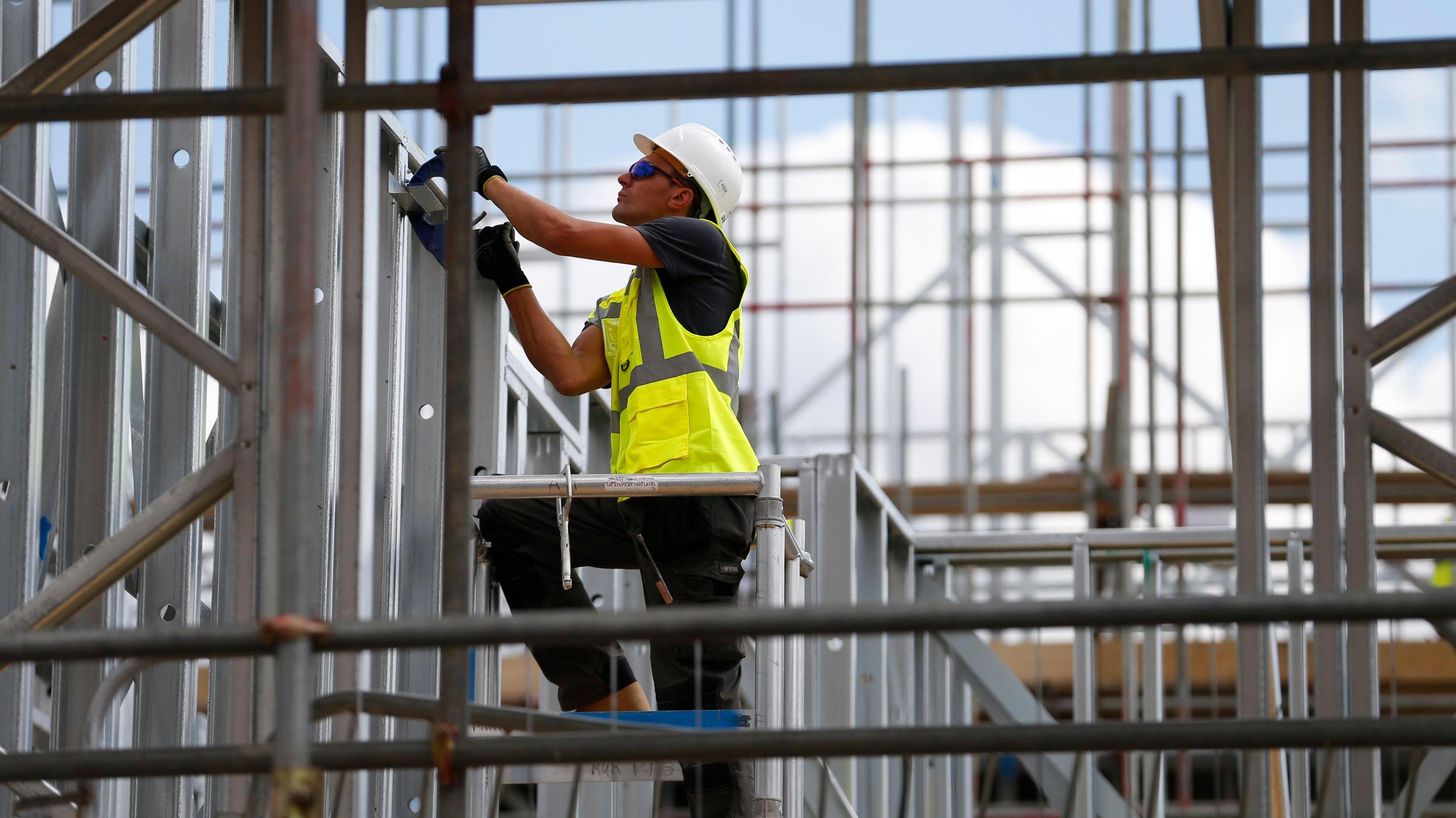 A male construction worker on a building site wearing a hard hat and a yellow high visibility jacket