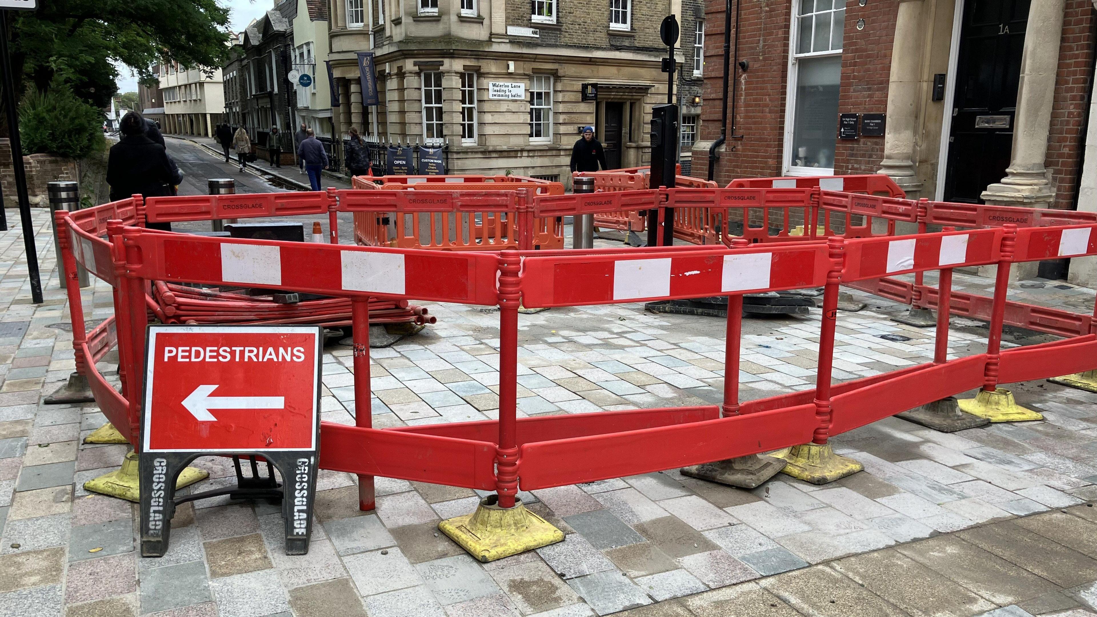 Bright red roadworks with a smalls sign with an arrow to the walkway. It says "pedestrians".