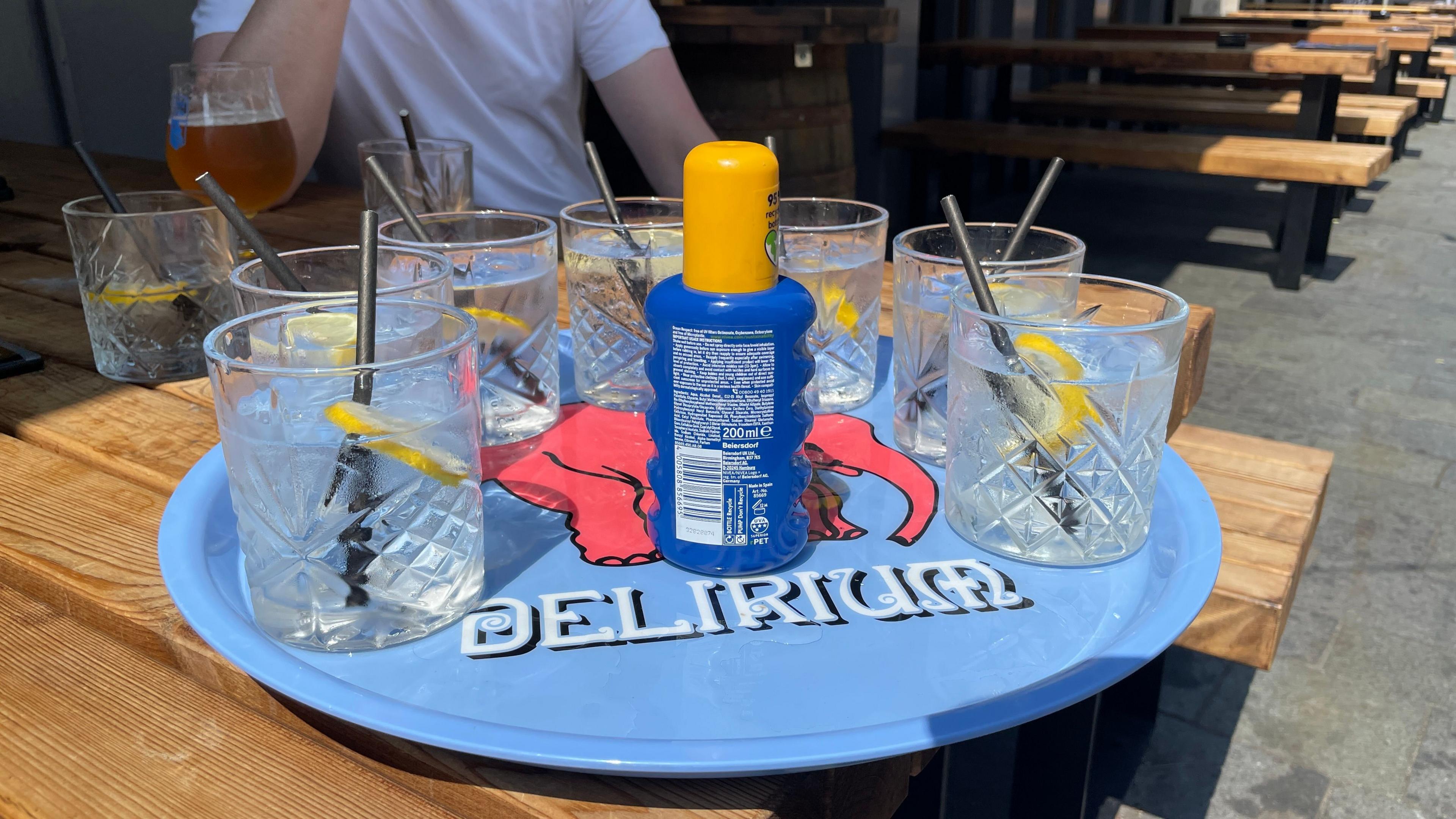 A blue tray with suncream and glasses of water on for customers to use. The tray is on a picnic bench in the beer garden of the Head of Steam pub in Sheffield city centre.