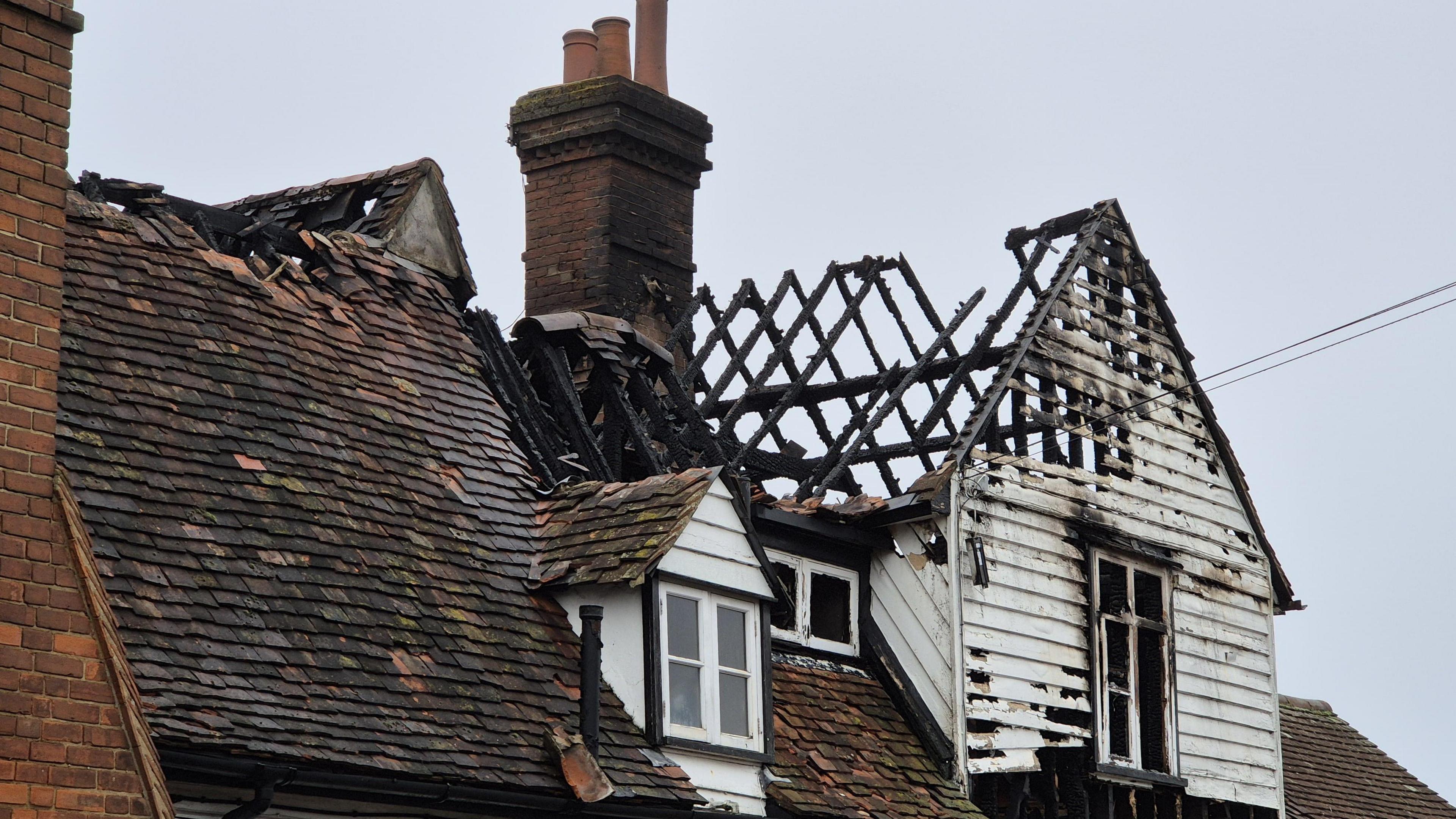 Part of a roof of an old pub. The roof has collapsed on one side, with only charred joists remaining